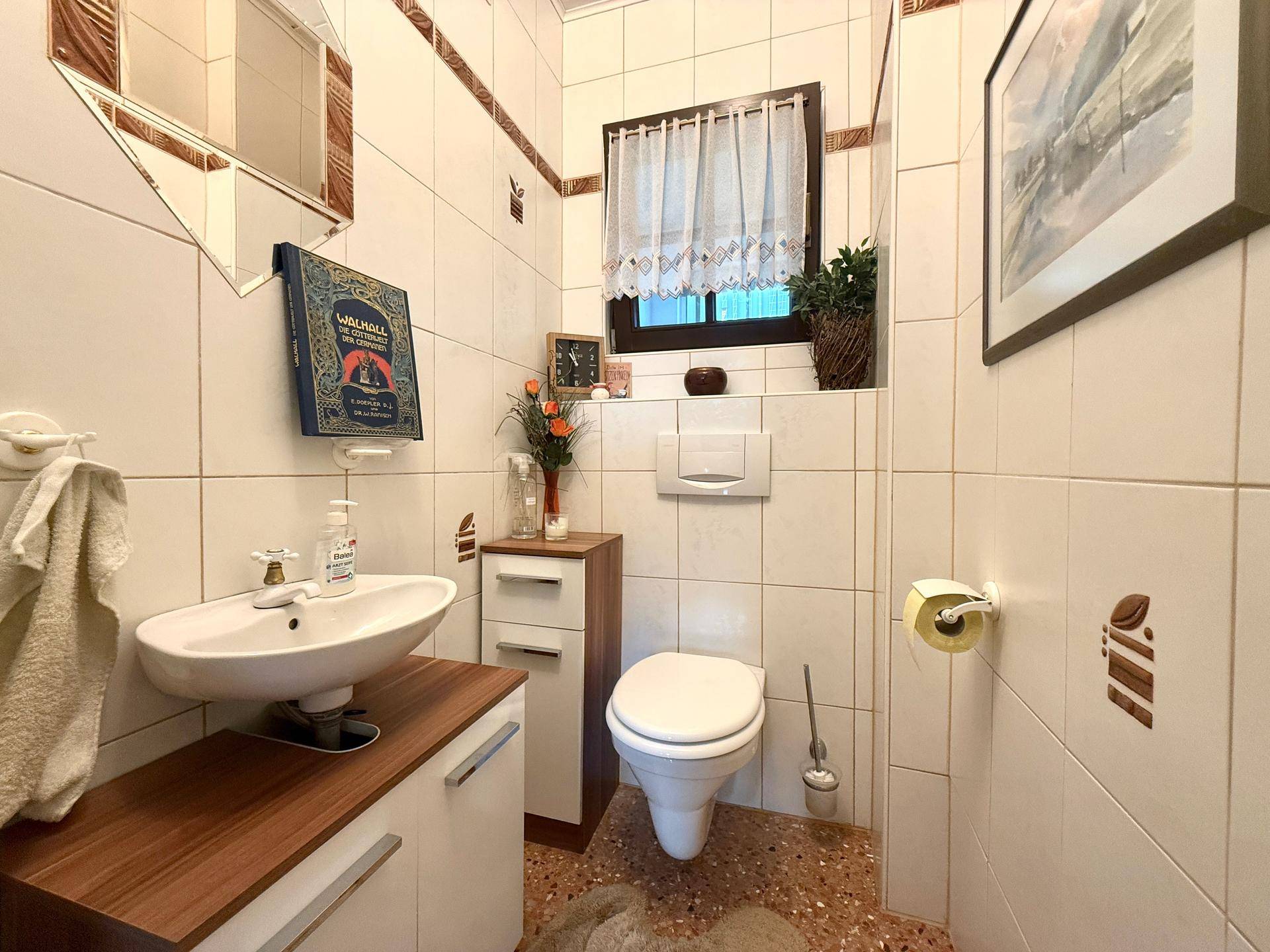 Kleines Gäste-WC mit Toilette, Waschbecken und Fenster, hell gefliest mit dezenten Akzenten.