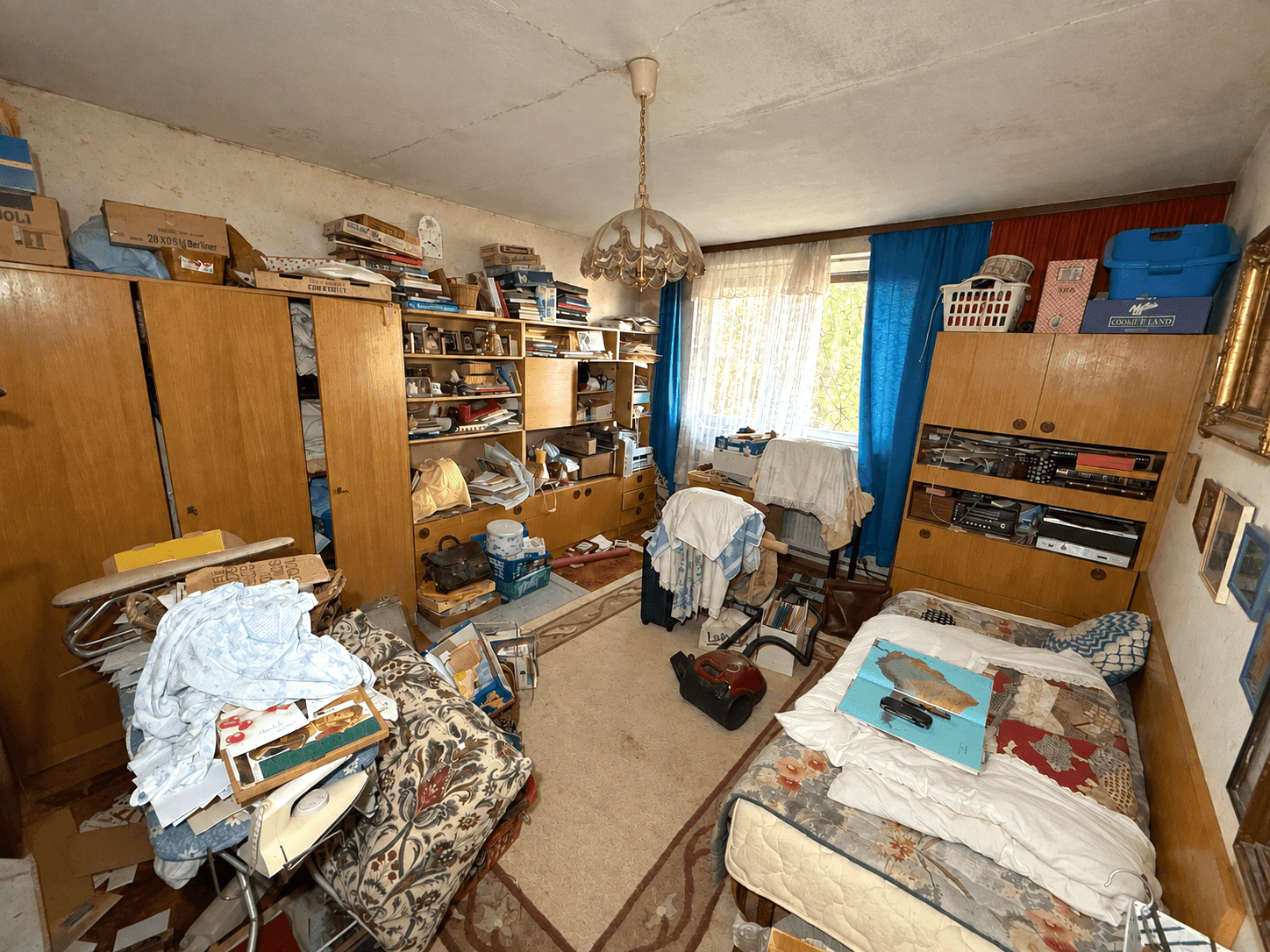 Schlafzimmer mit Einzelbett, Schränken und Teppichboden, viele persönliche Gegenstände.