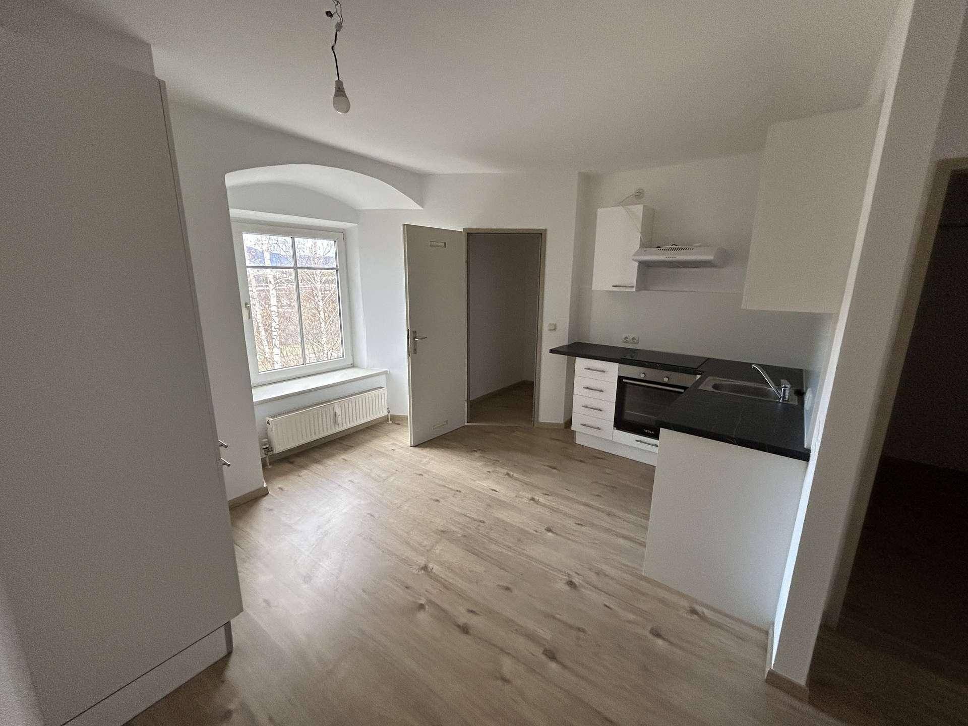 Funktionale Küchenzeile mit weißen Schränken und Laminatboden in einem hellen Raum mit Fenster.