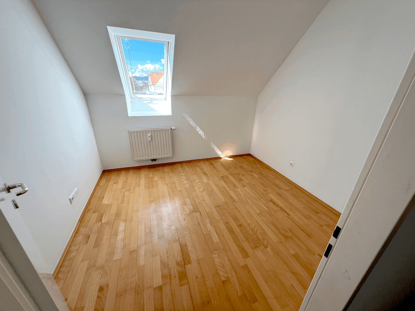 Gemütliches Schlafzimmer mit Holzboden, Dachfenster und Blick auf die umliegenden Dächer.