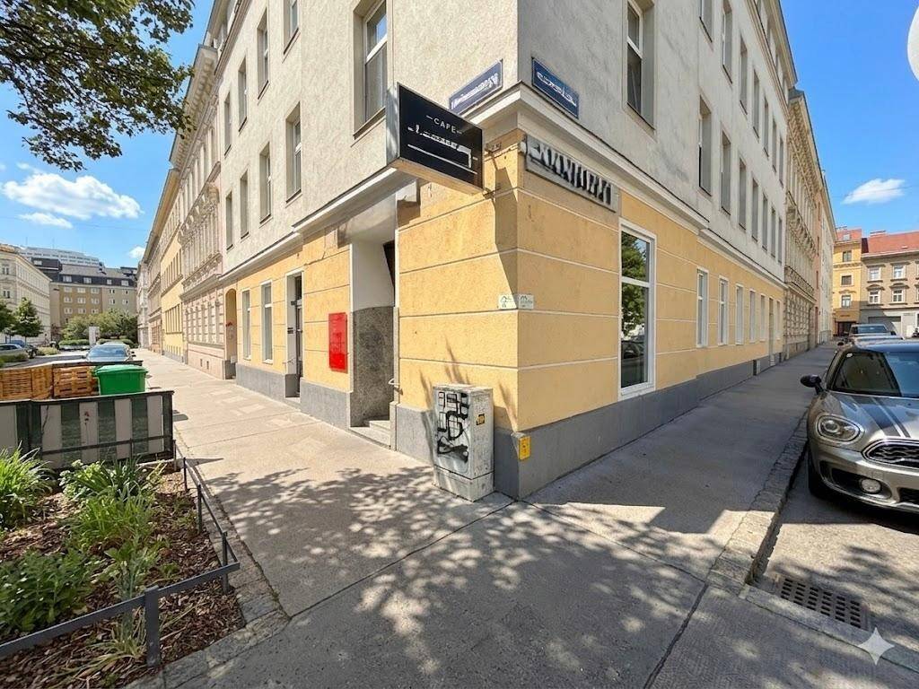 Gelbes Eckgebäude mit großen Fenstern und einem Geschäft im Erdgeschoss an einer Straße.