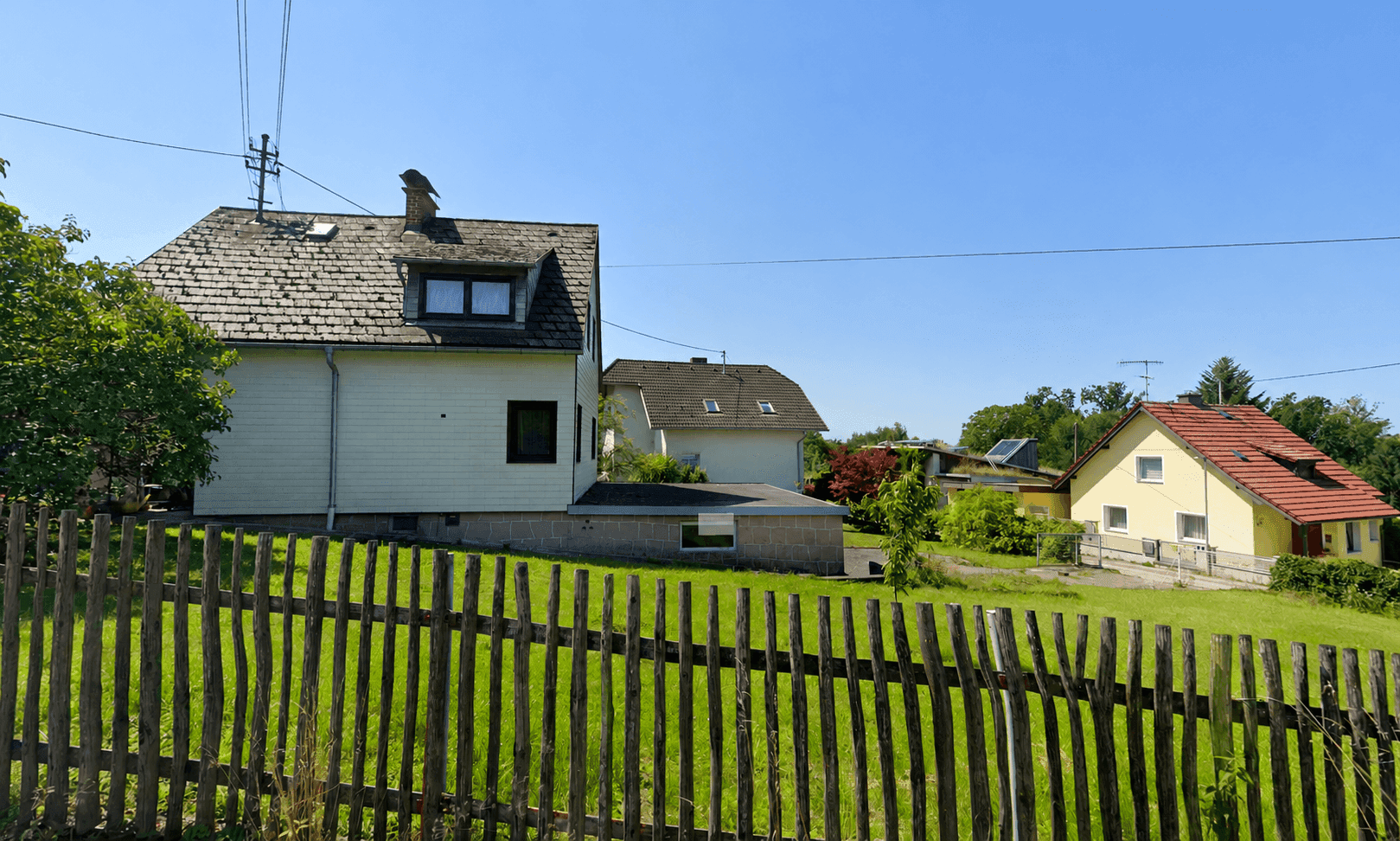 Rückansicht des Hauses mit Garten, Holzzaun und weiteren Gebäuden in ländlicher Umgebung.