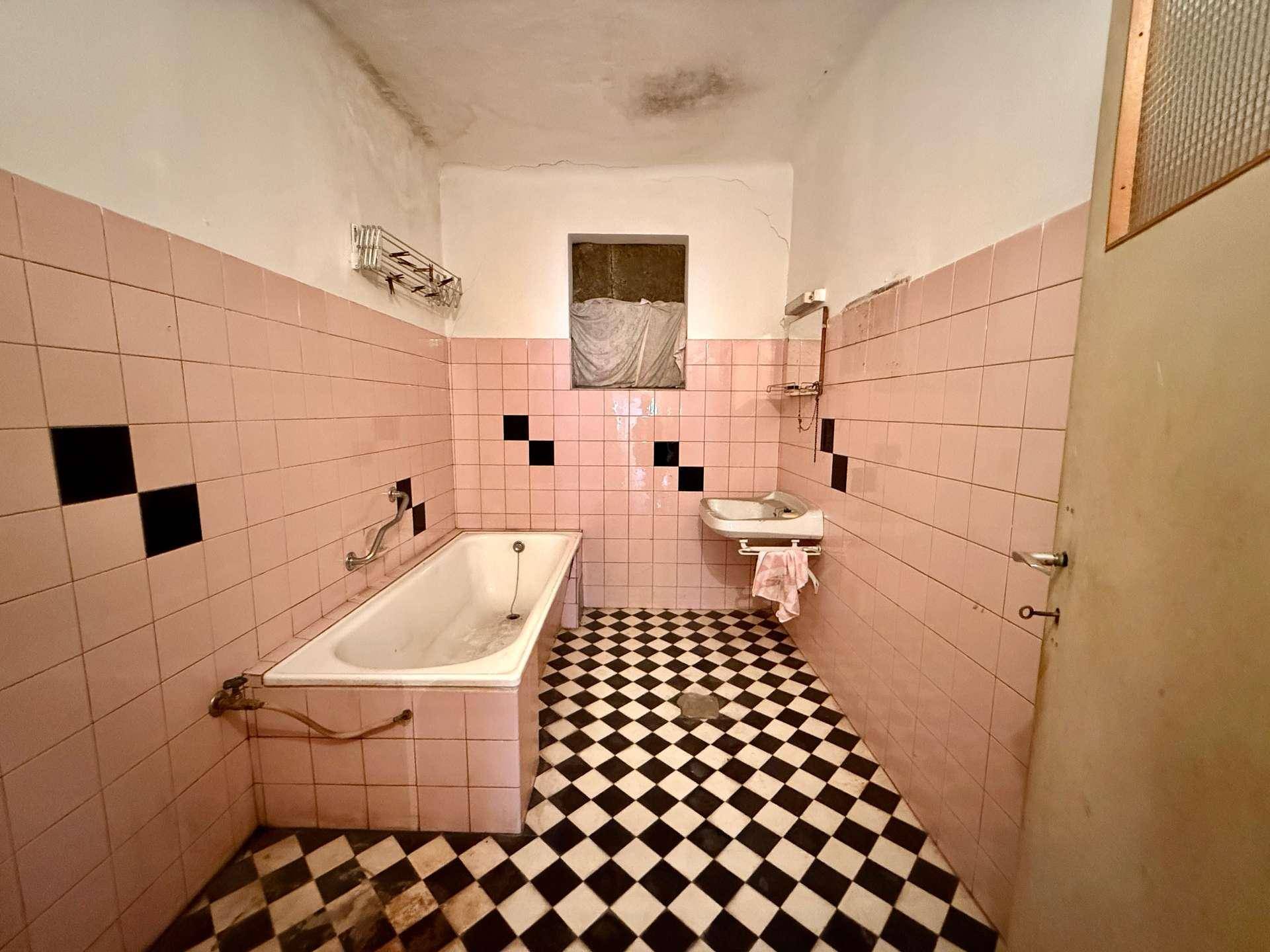 Badezimmer im Stil der 80er Jahre mit rosa Wandfliesen, kariertem Boden und Badewanne.