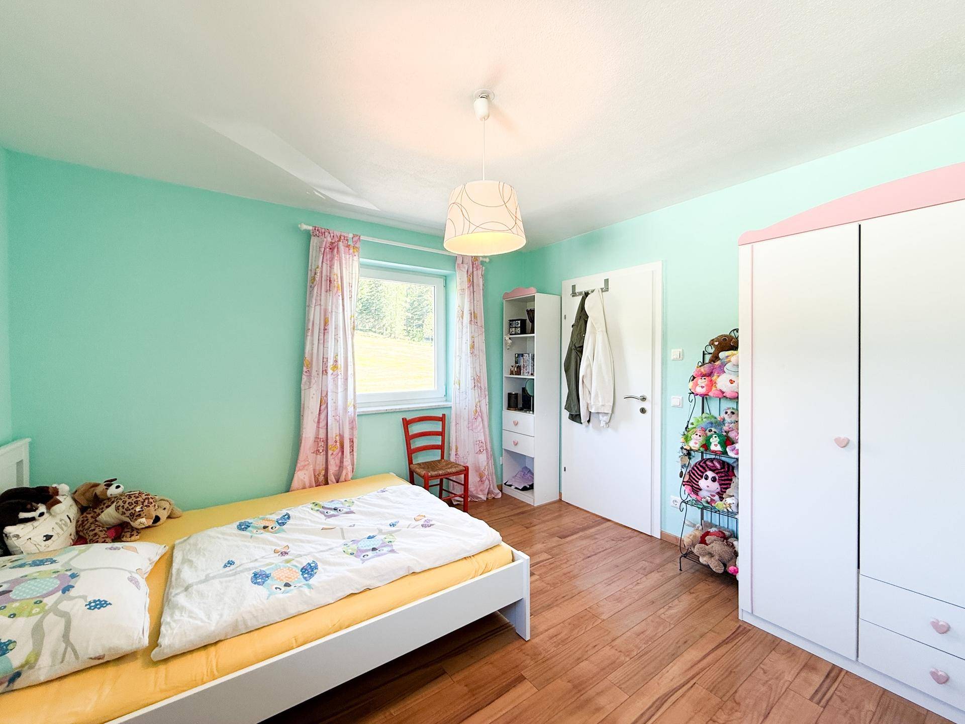 Helles Kinderzimmer mit mintgrünen Wänden, Holzboden und Blick ins Grüne.