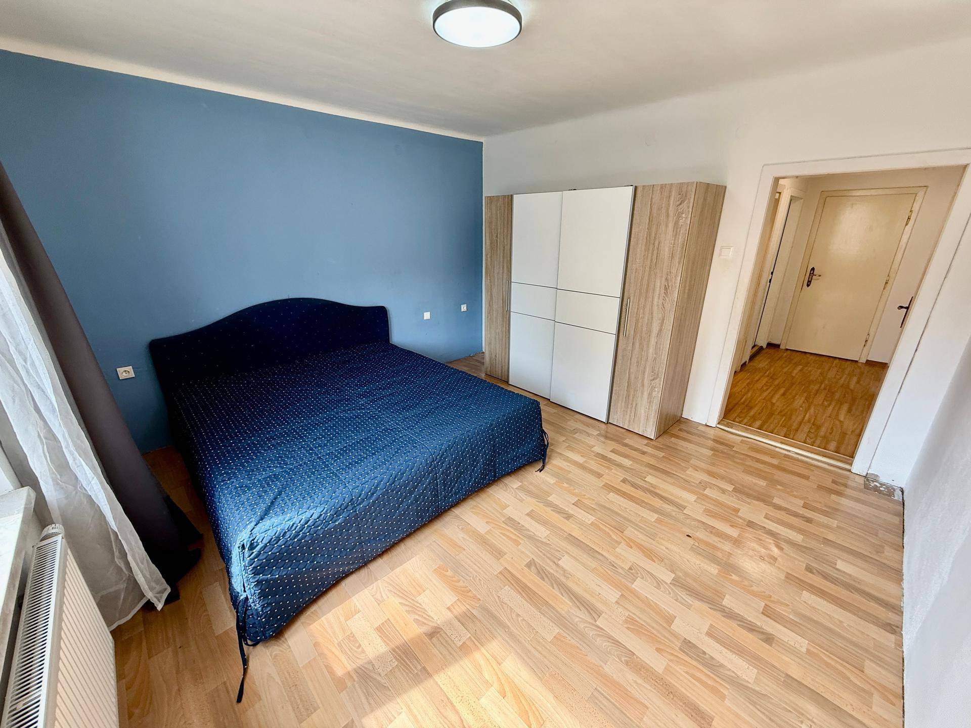Schlafzimmer mit blauer Akzentwand, Holzboden und einem Doppelbett.