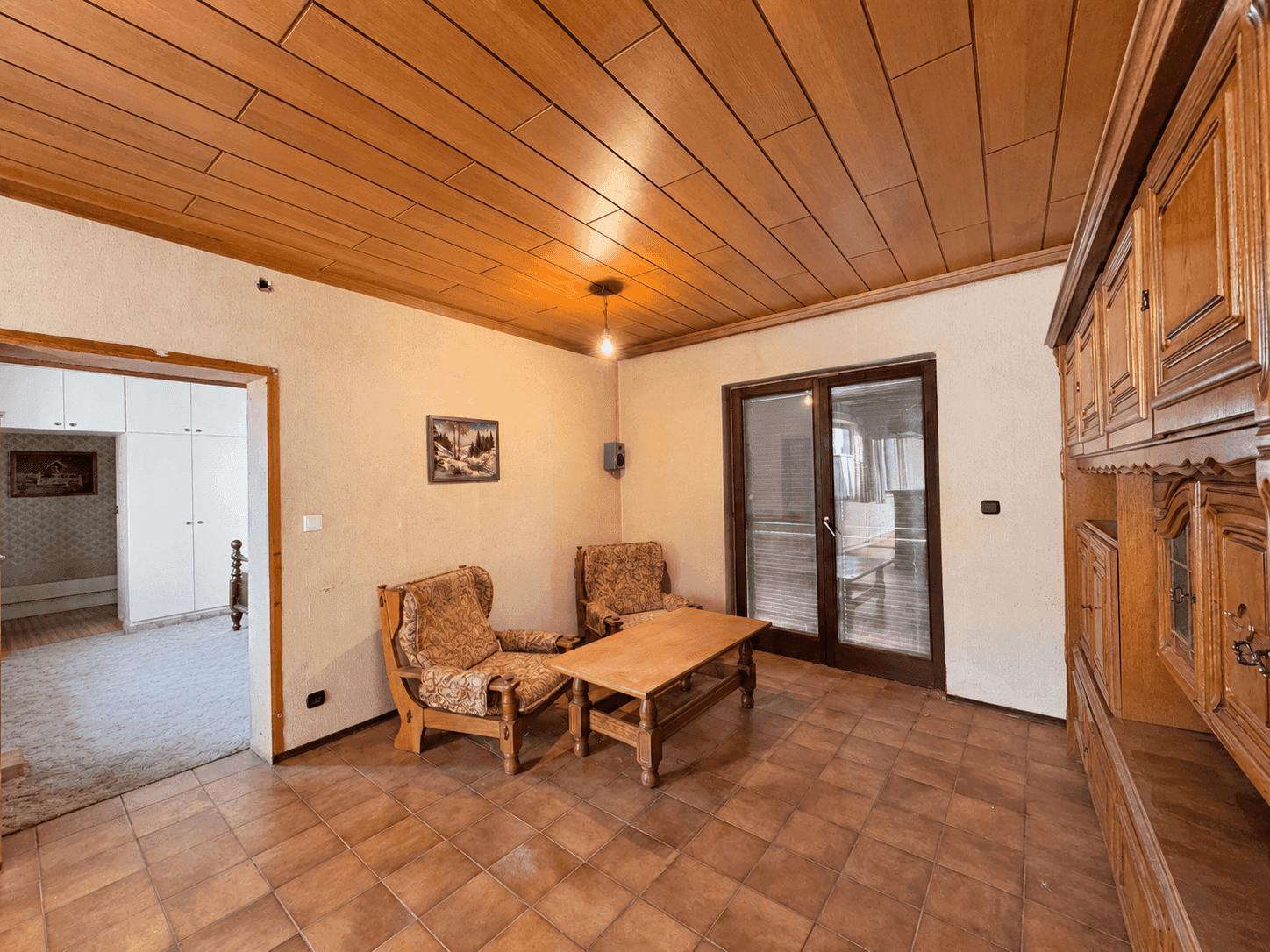 Gemütliches Wohnzimmer mit Holzdecke, Fliesenboden und Zugang zum Außenbereich.