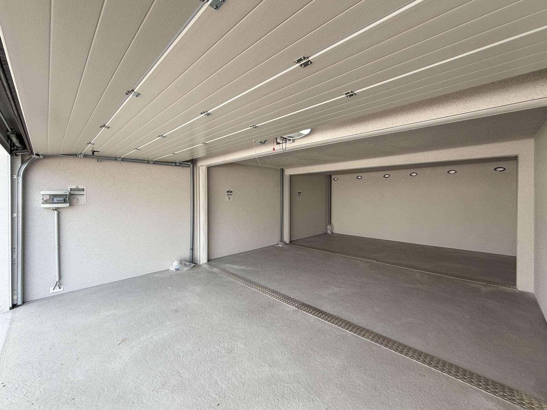 Geräumige Garagenbox mit Betonboden und Wandinstallationen, ideal für Fahrzeuge.