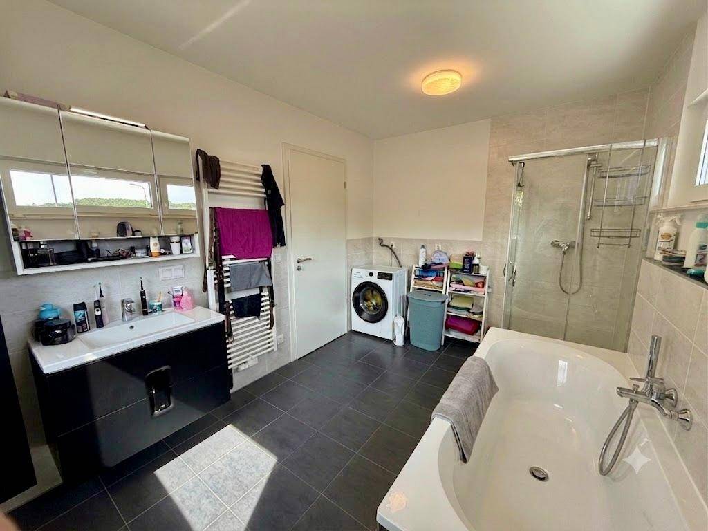 Funktionales Badezimmer mit Waschmaschine, Badewanne, Dusche und beheiztem Handtuchhalter.
