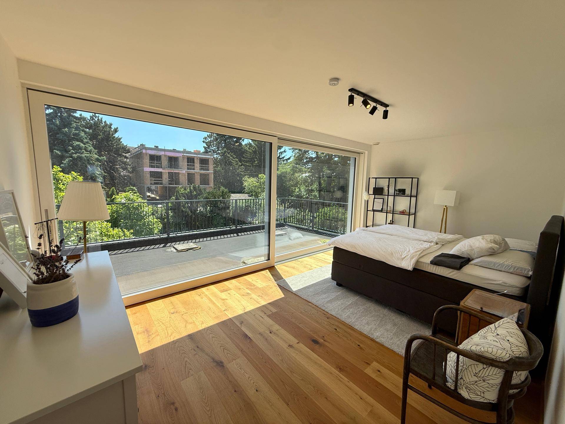 Schlafzimmer mit Holzboden, großzügigen Fenstern und direktem Zugang zur Dachterrasse.