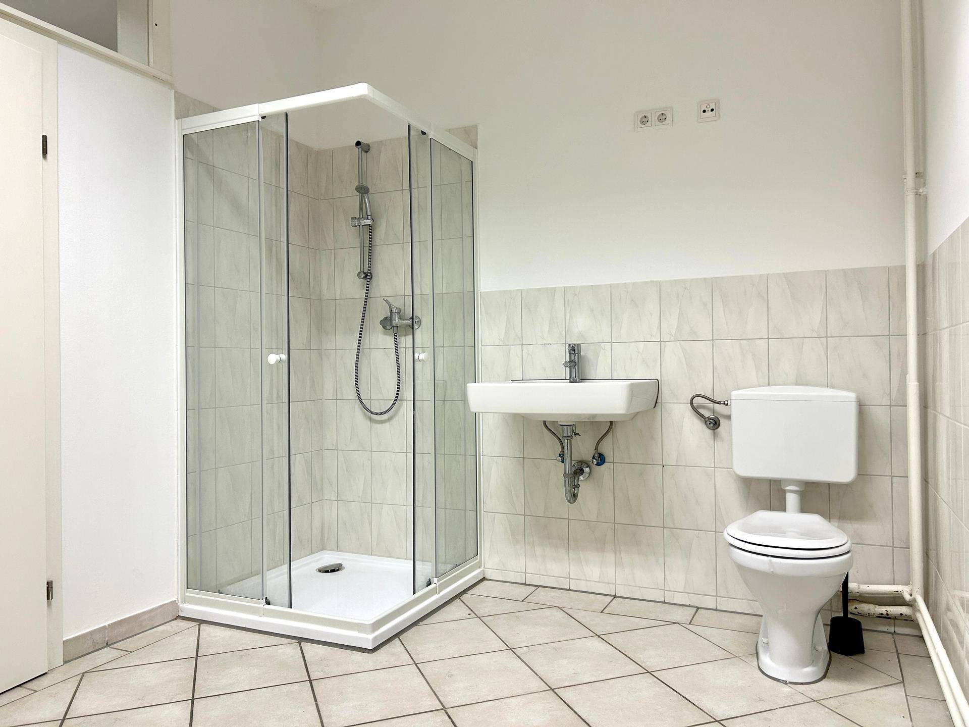 Funktionales Badezimmer mit Duschkabine, Toilette und Waschbecken auf Fliesenboden.