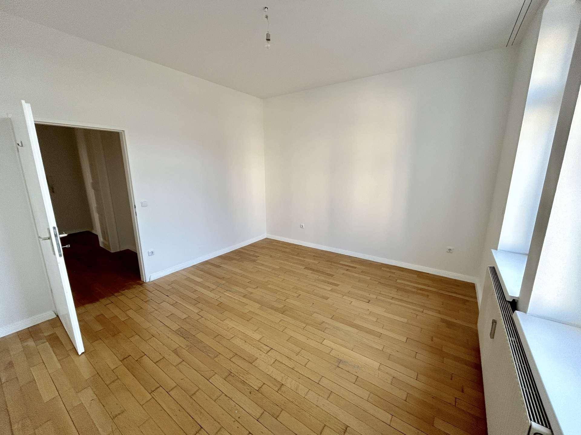 Helles Zimmer mit Holzboden und weiß gestrichenen Wänden, bereit zur individuellen Gestaltung.