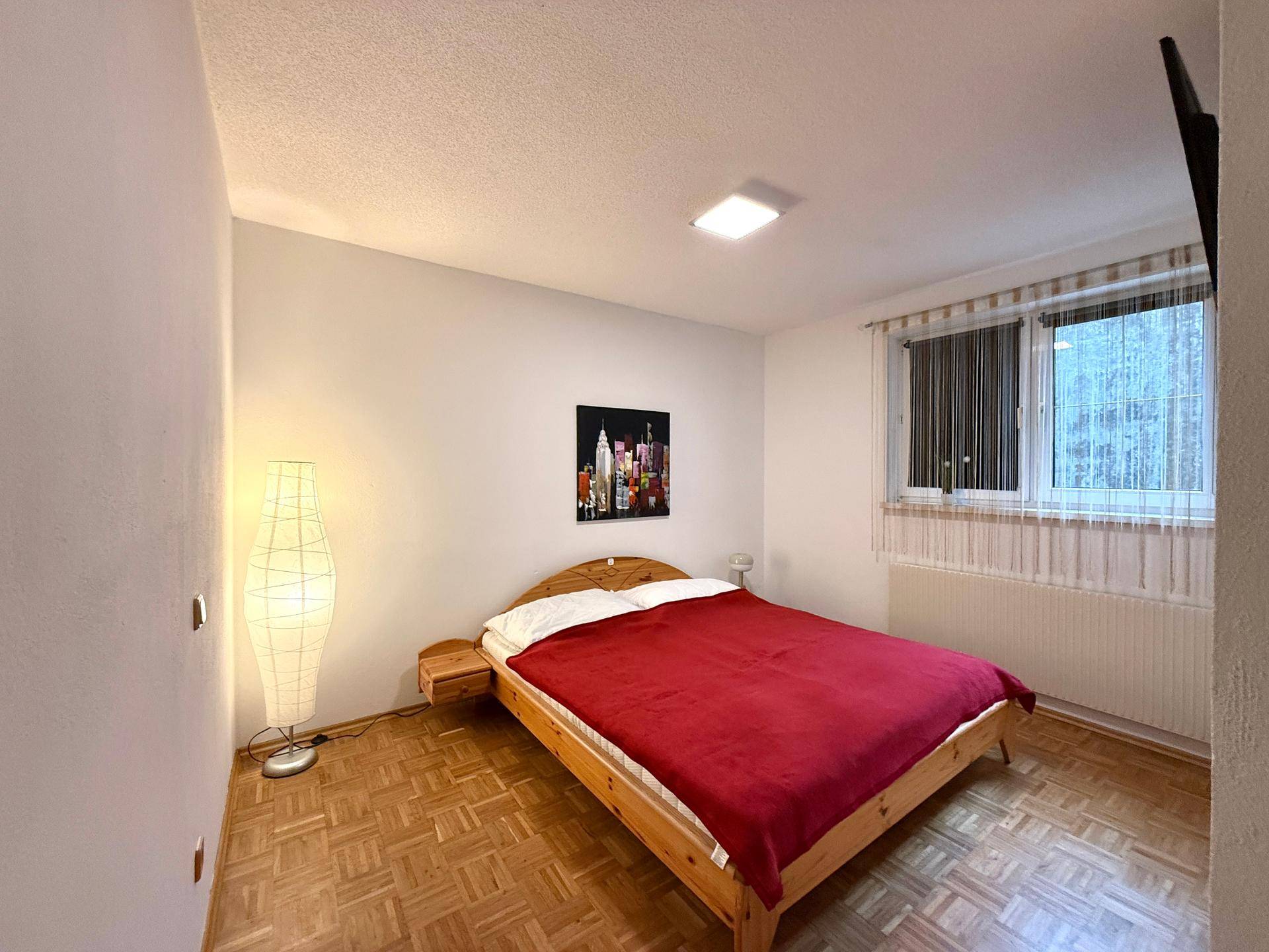 Schlafzimmer mit Parkettboden, Doppelbett und Fenster mit Blick nach draußen.