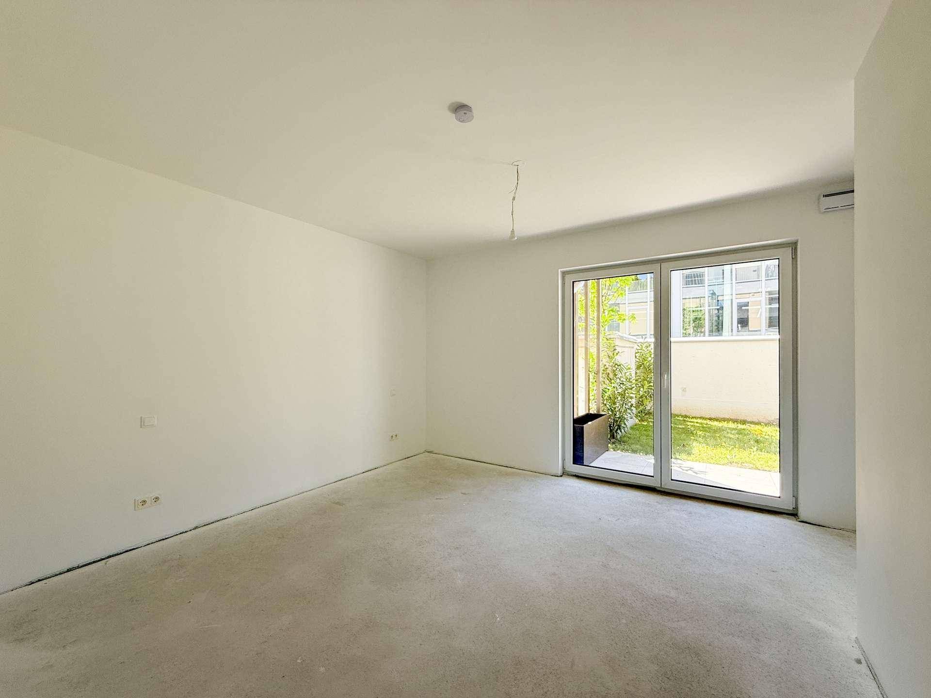 Helles Schlafzimmer im Rohbau mit großem Fenster und direktem Gartenzugang.