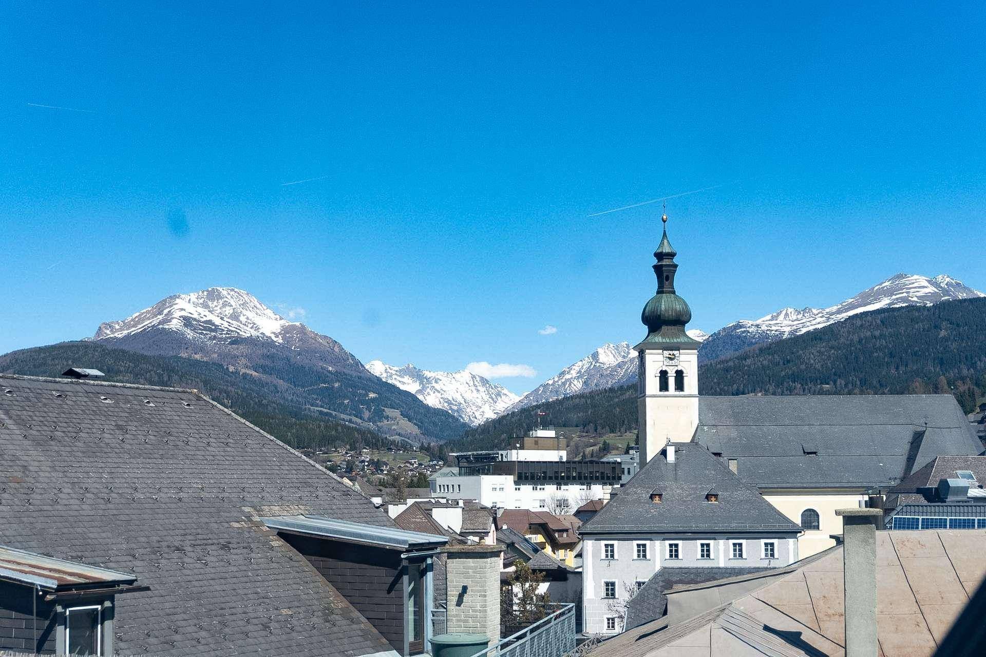 Weitblick über eine charmante Stadt mit Kirchturm und majestätischen schneebedeckten Bergen am Horizont.