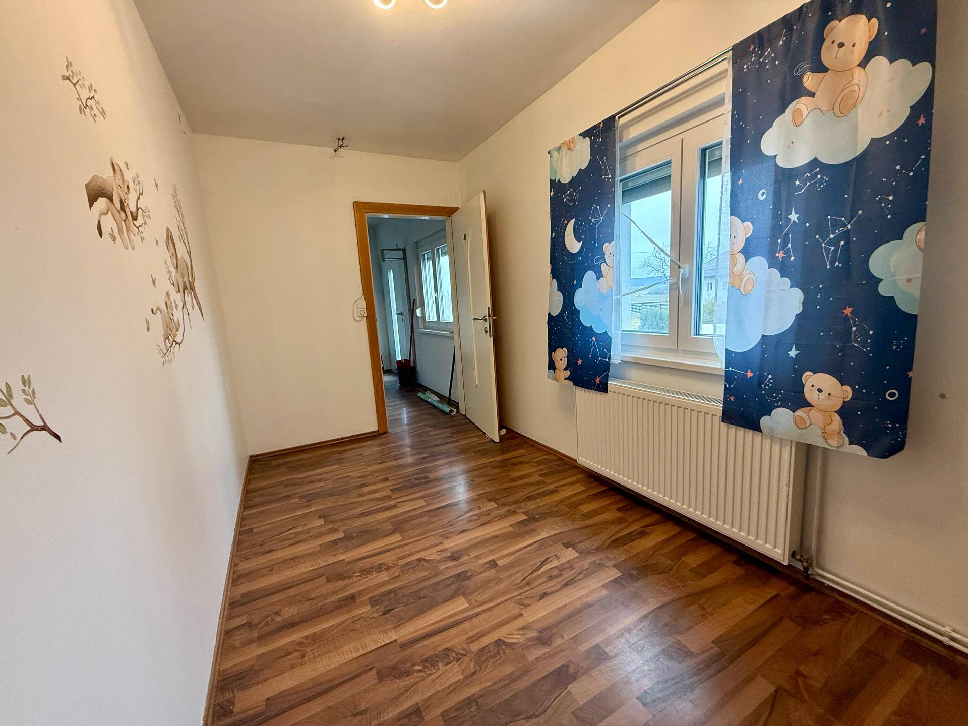 Kinderzimmer mit Holzboden, Fenster und verspielten Vorhängen mit Bärenmotiv.