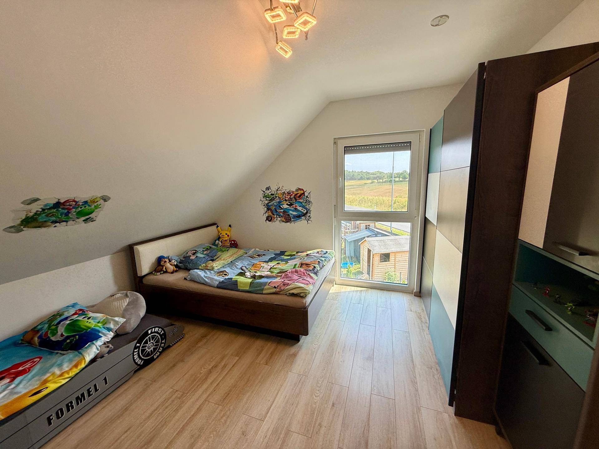 Freundliches Kinderzimmer mit Bett, Kleiderschrank und Blick ins Freie.