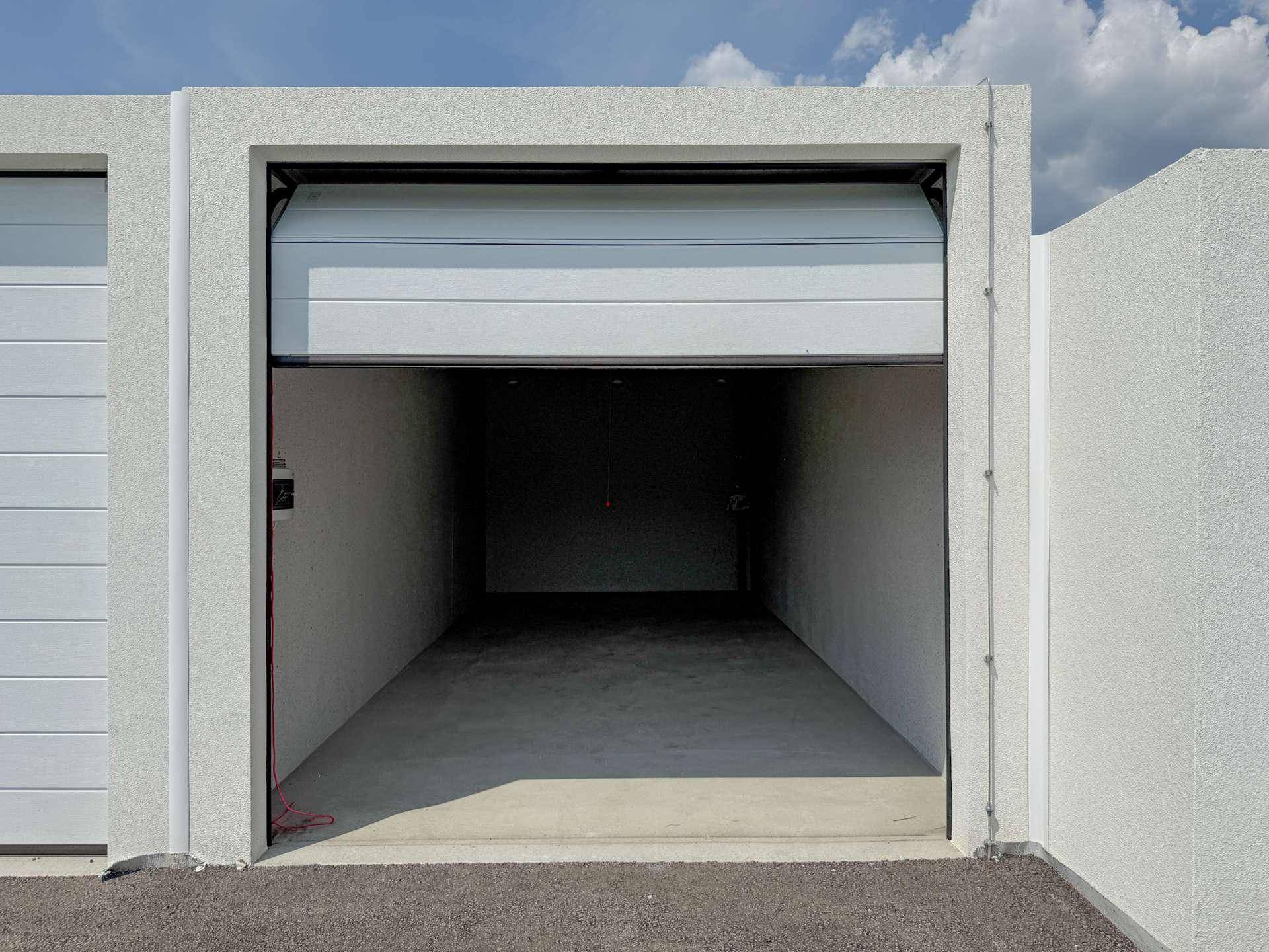Eine moderne Garagenbox mit weißem Rolltor, das sich teilweise schließt, unter blauem Himmel.