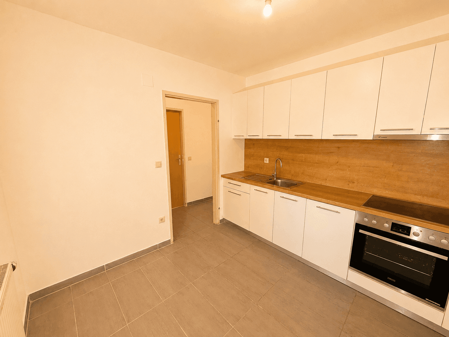Moderne Küche mit weißen Schränken, Holzarbeitsplatten, Spüle, Backofen und Induktionskochfeld.