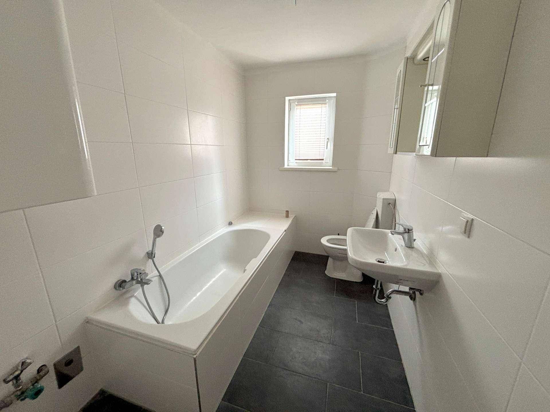 Gefliestes Badezimmer mit Badewanne, WC, Waschbecken und einem Fenster für Tageslicht.