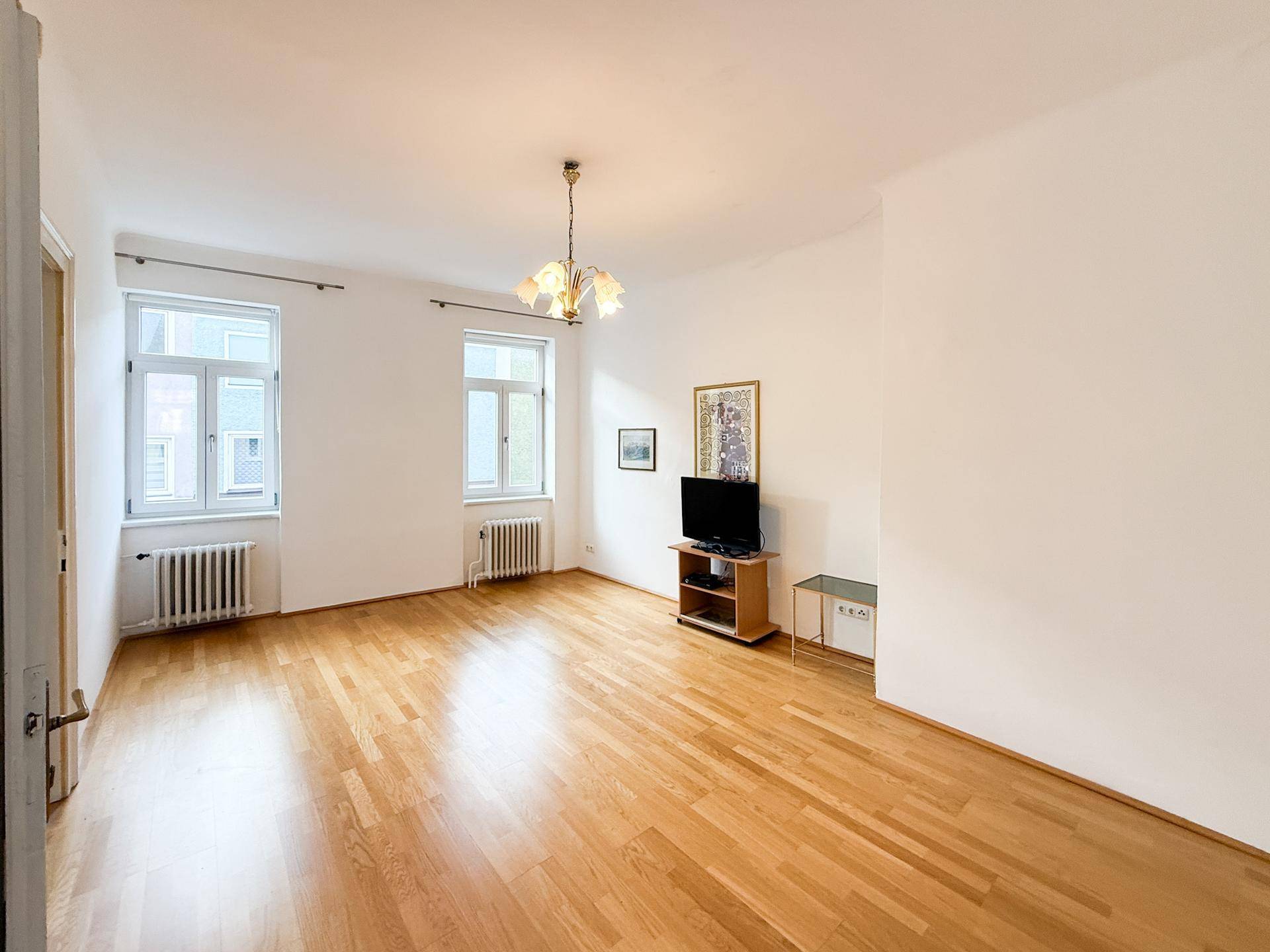 Leeres Wohnzimmer mit Holzboden, hohen Decken und zwei großen Fenstern.