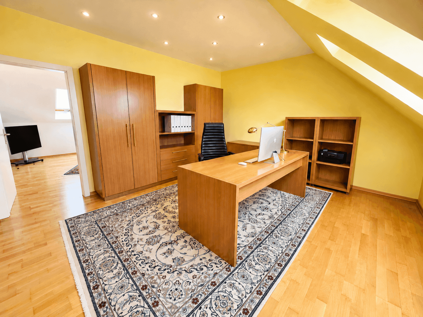 Helles Arbeitszimmer im Dachgeschoss mit Holzmöbeln, Parkettboden und Dachfenstern.