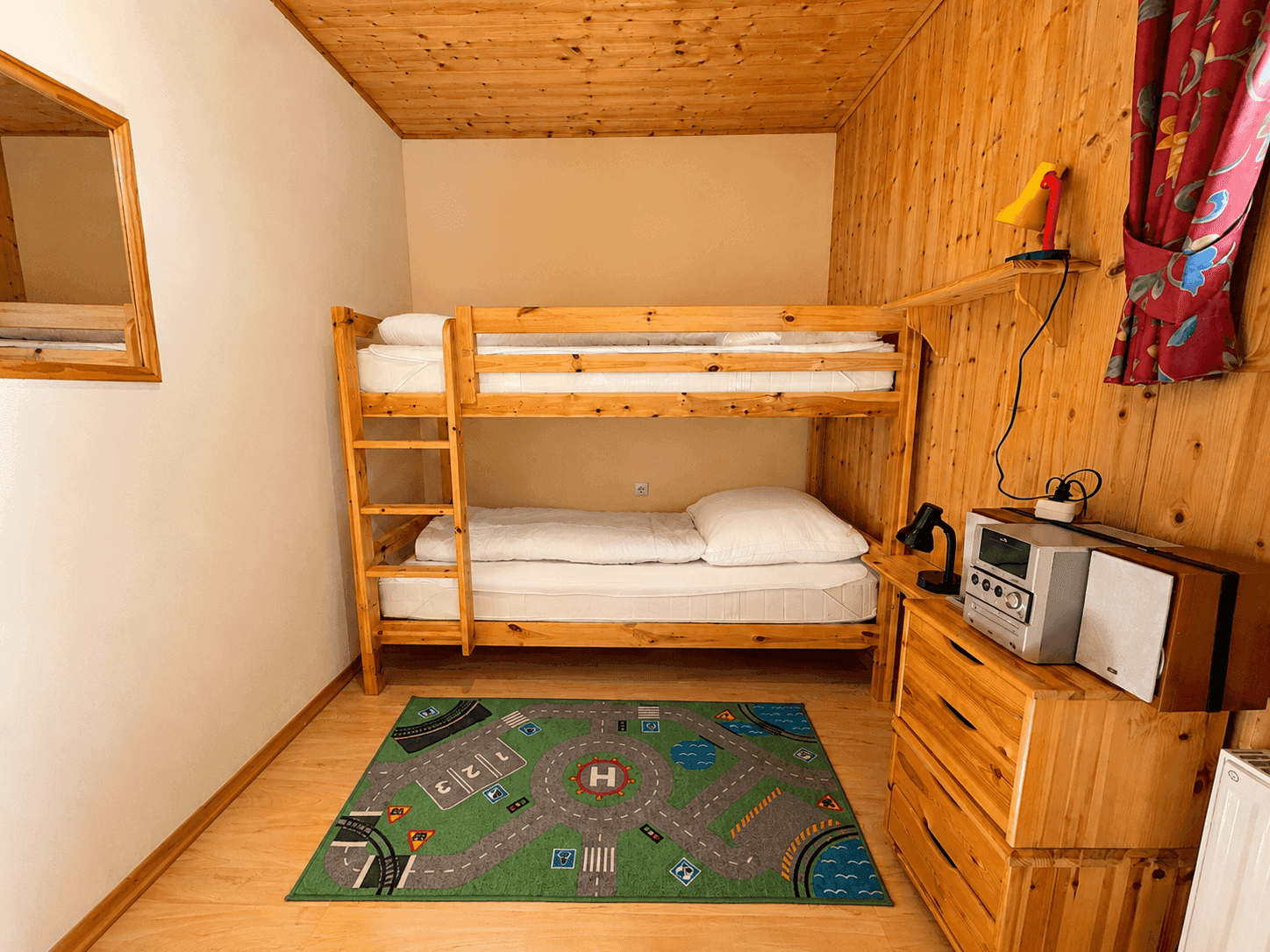 Kinderzimmer mit Etagenbett aus Holz, Spielteppich und Holzvertäfelung an einer Wand.