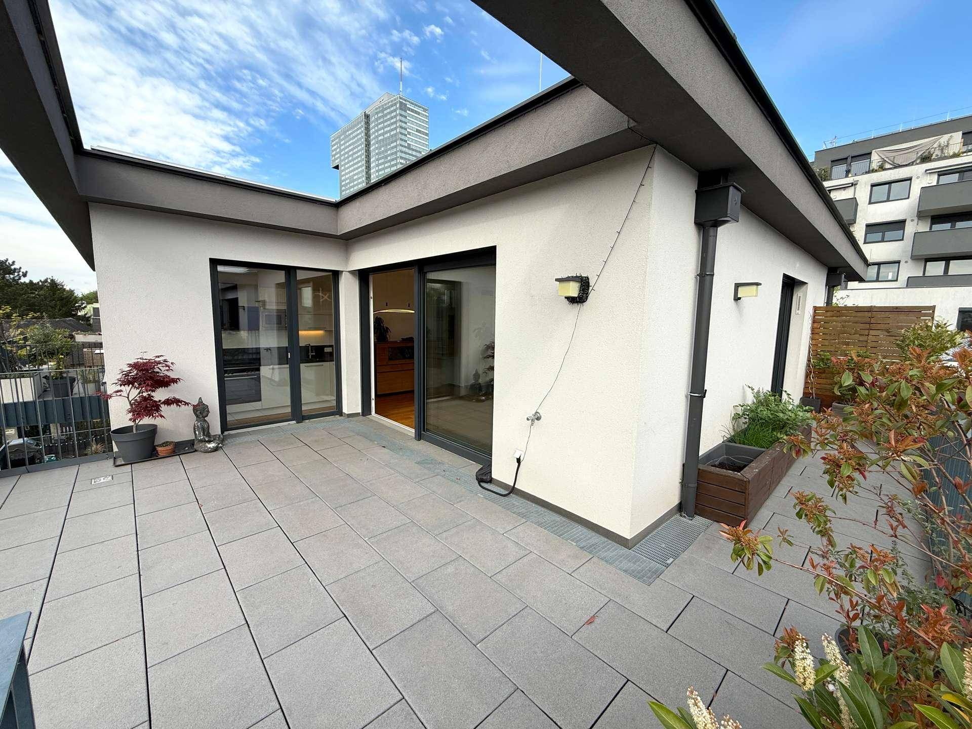 Moderne Gebäudefassade mit großer, gefliester Terrasse und Blick auf die umliegende Bebauung.