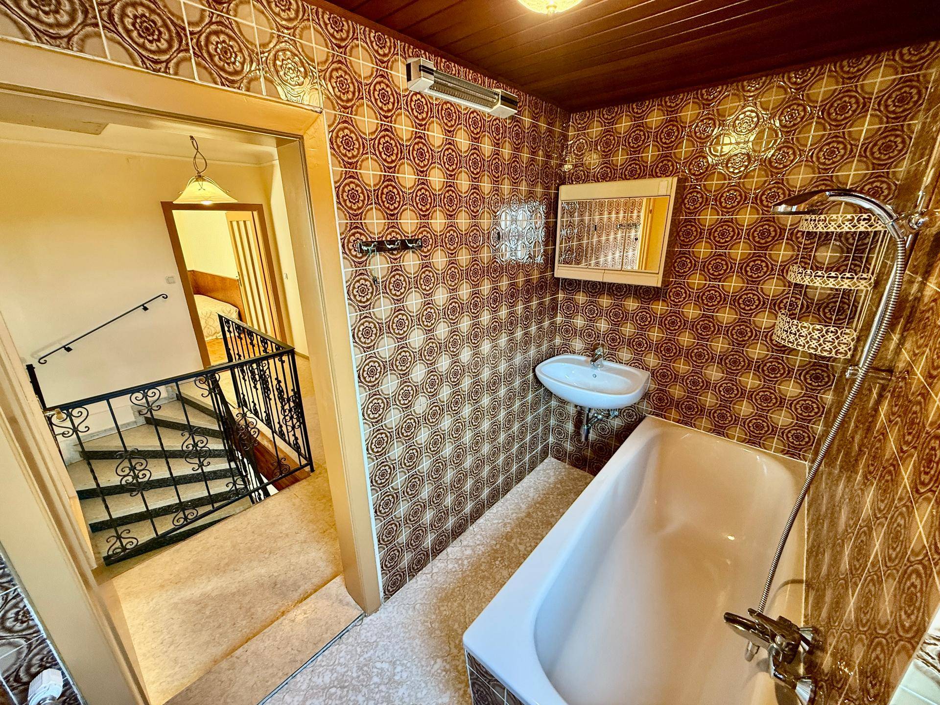Badezimmer im 80er-Jahre-Stil mit Badewanne, Waschbecken und gemusterten Fliesen.