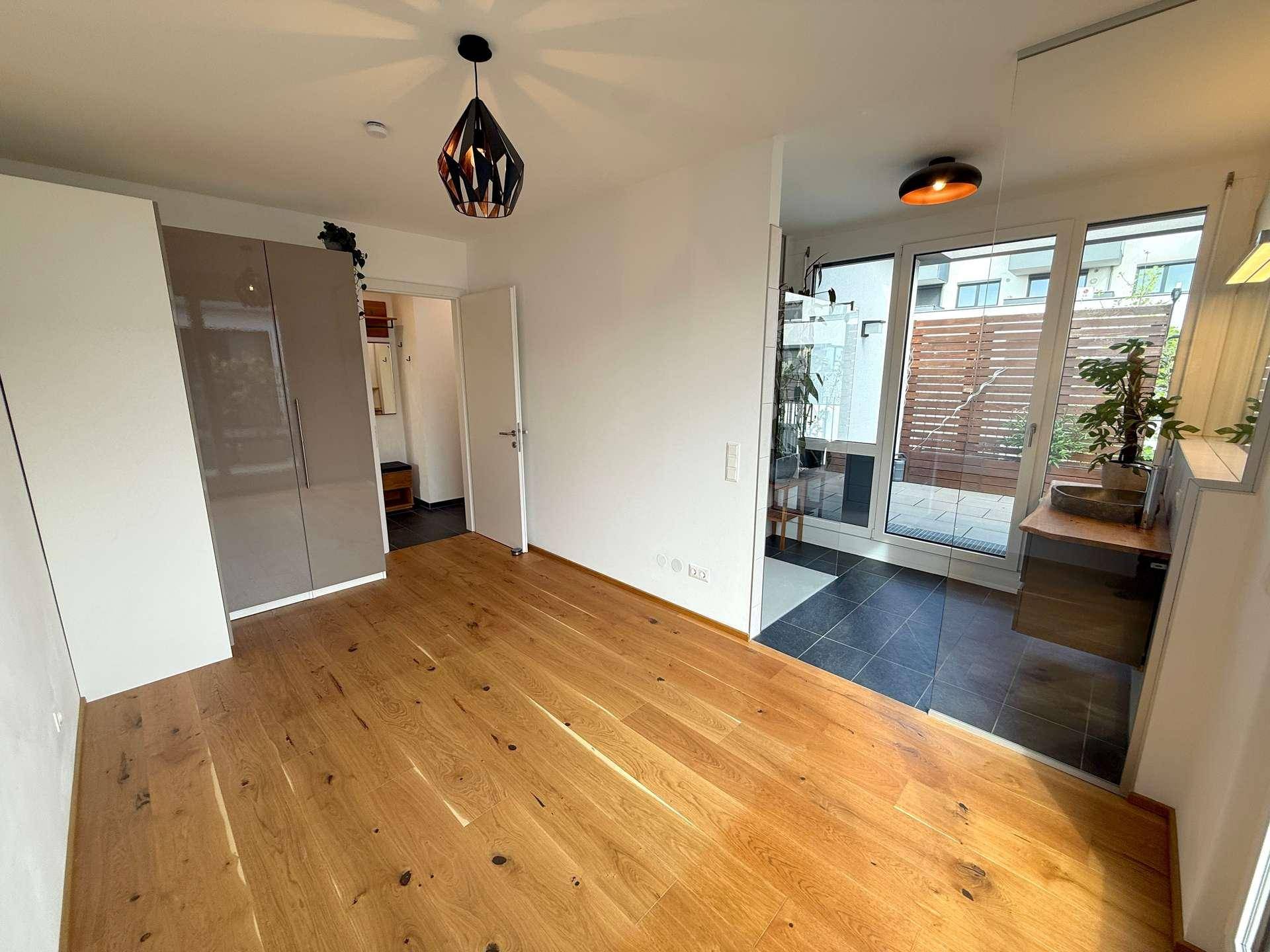 Schlafzimmer mit Holzboden, Einbauschrank und Zugang zu einem Badezimmer sowie einem Außenbereich.