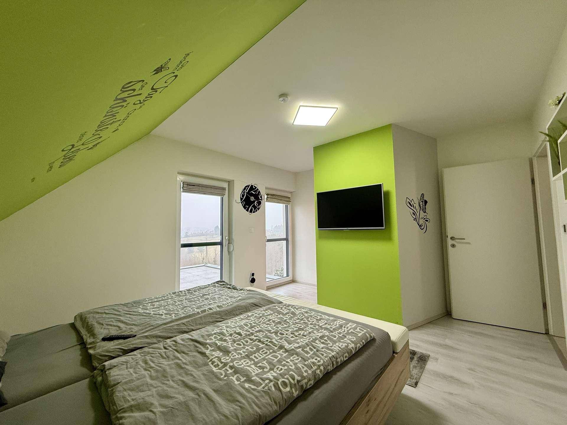 Schlafzimmer mit Doppelbett, grüner Akzentwand und Zugang zu einem Balkon oder Terrasse.