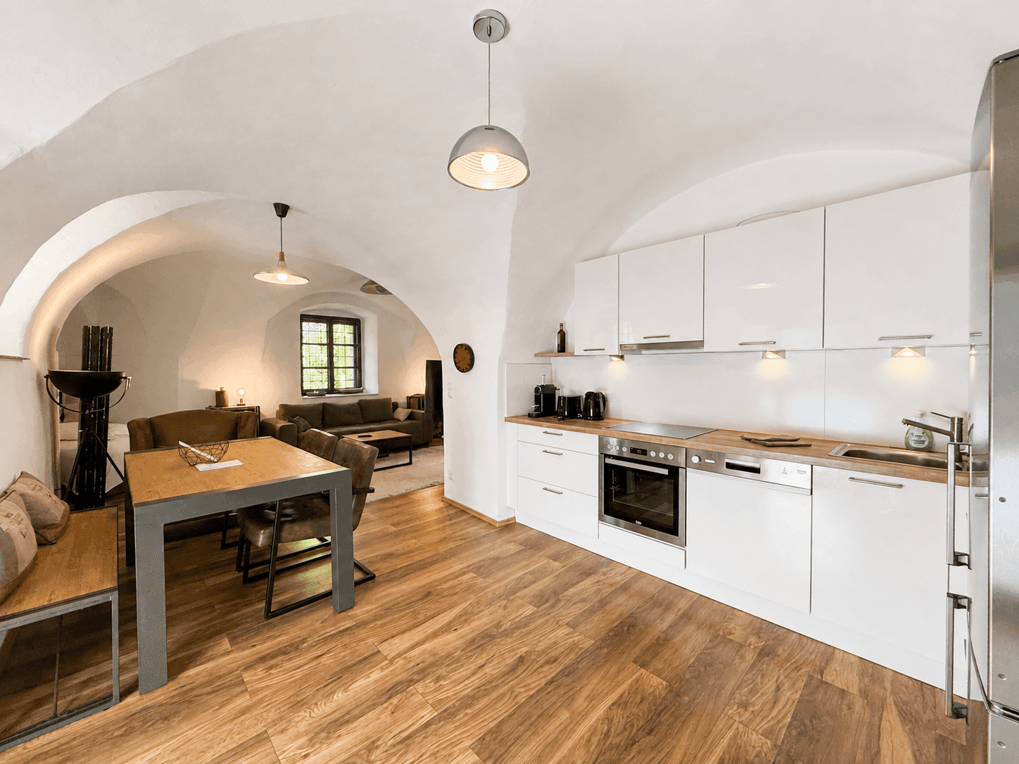 Moderne Einbauküche mit weißen Hochglanzfronten und Essbereich unter Gewölbedecken.