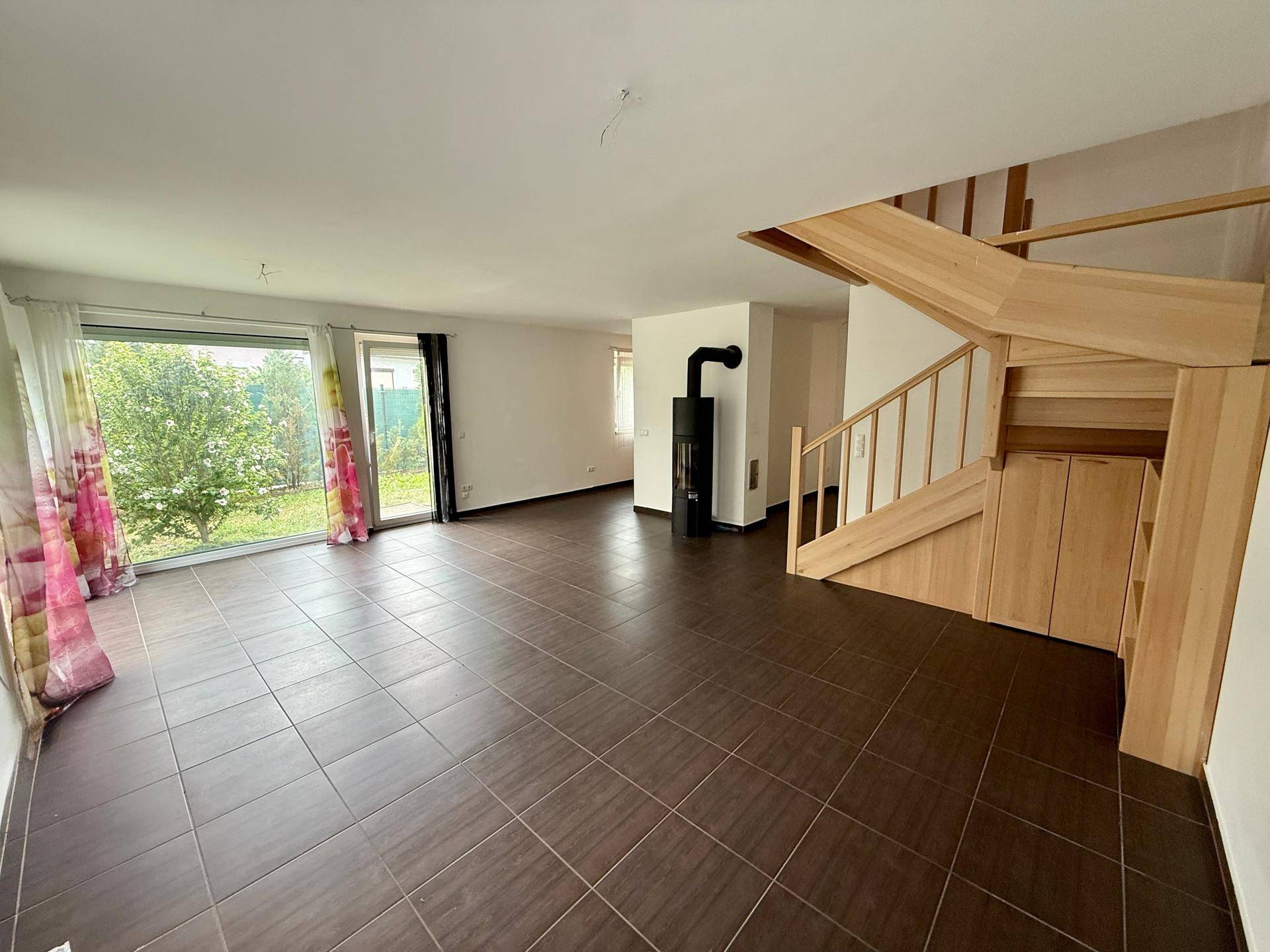 Geräumiges Wohnzimmer mit dunklen Fliesen, Holztreppe und einem modernen Kaminofen.