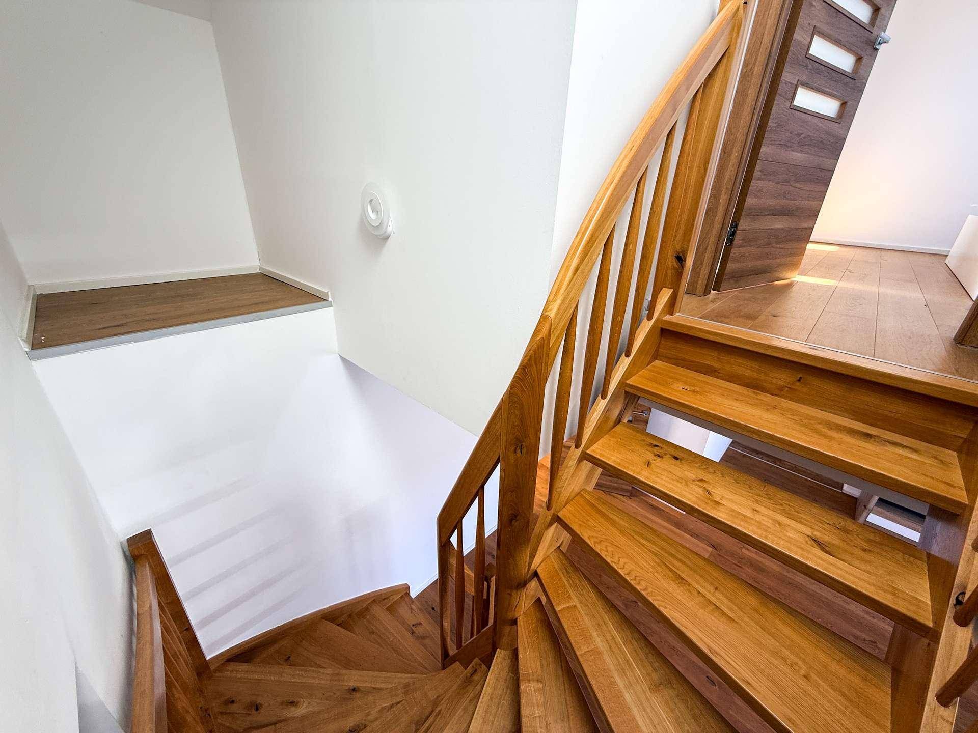 Elegante Holztreppe mit geschwungenem Geländer, die die verschiedenen Ebenen des Hauses verbindet.