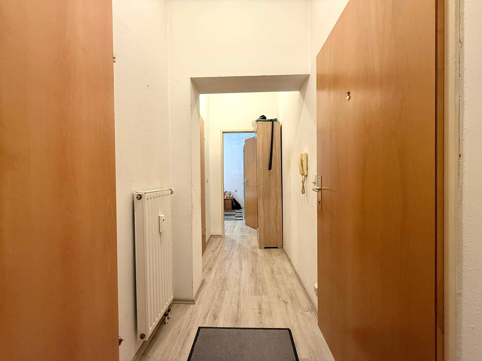 Heller Flur mit Laminatboden, Holztüren und Heizkörper, der zu weiteren Räumen führt.