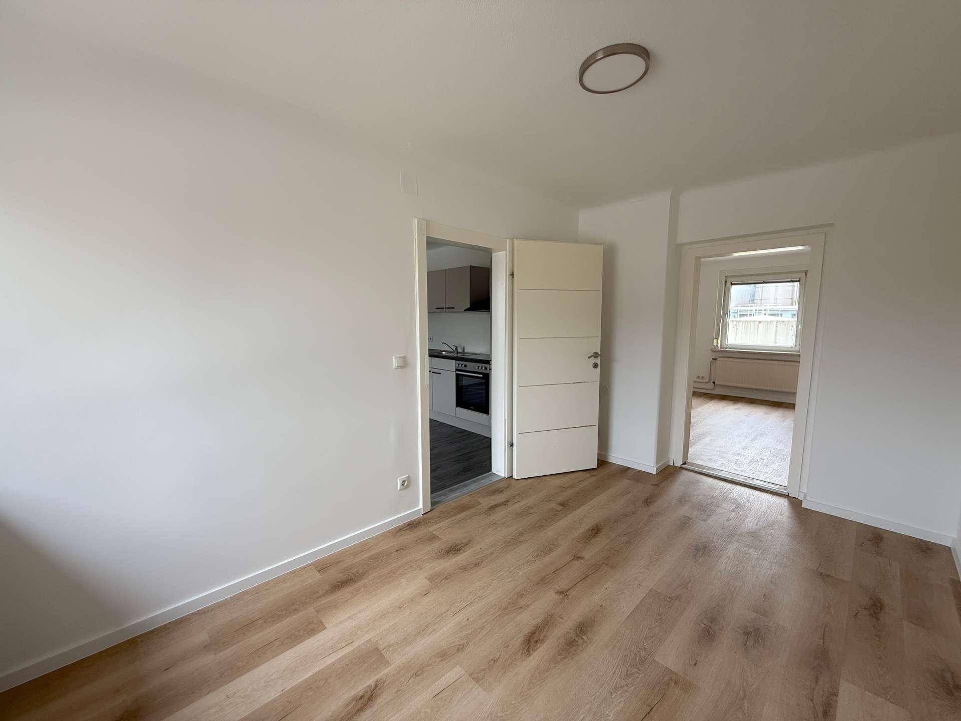 Heller Wohnbereich mit hellem Laminatboden und Zugang zur Küche sowie einem weiteren Zimmer.