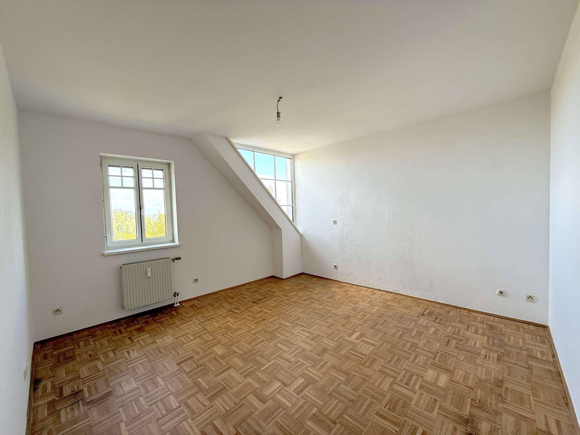 Geräumiges, unmöbliertes Wohnzimmer mit Parkettboden und Dachschrägen, bereit zur individuellen Gestaltung.