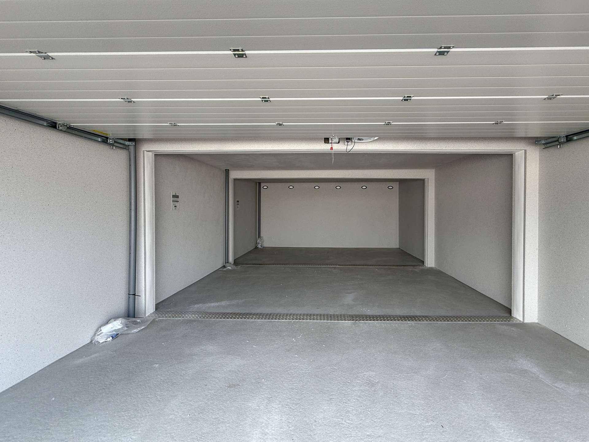 Innenansicht einer leeren Garagenbox mit Betonboden und Deckenbeleuchtung.