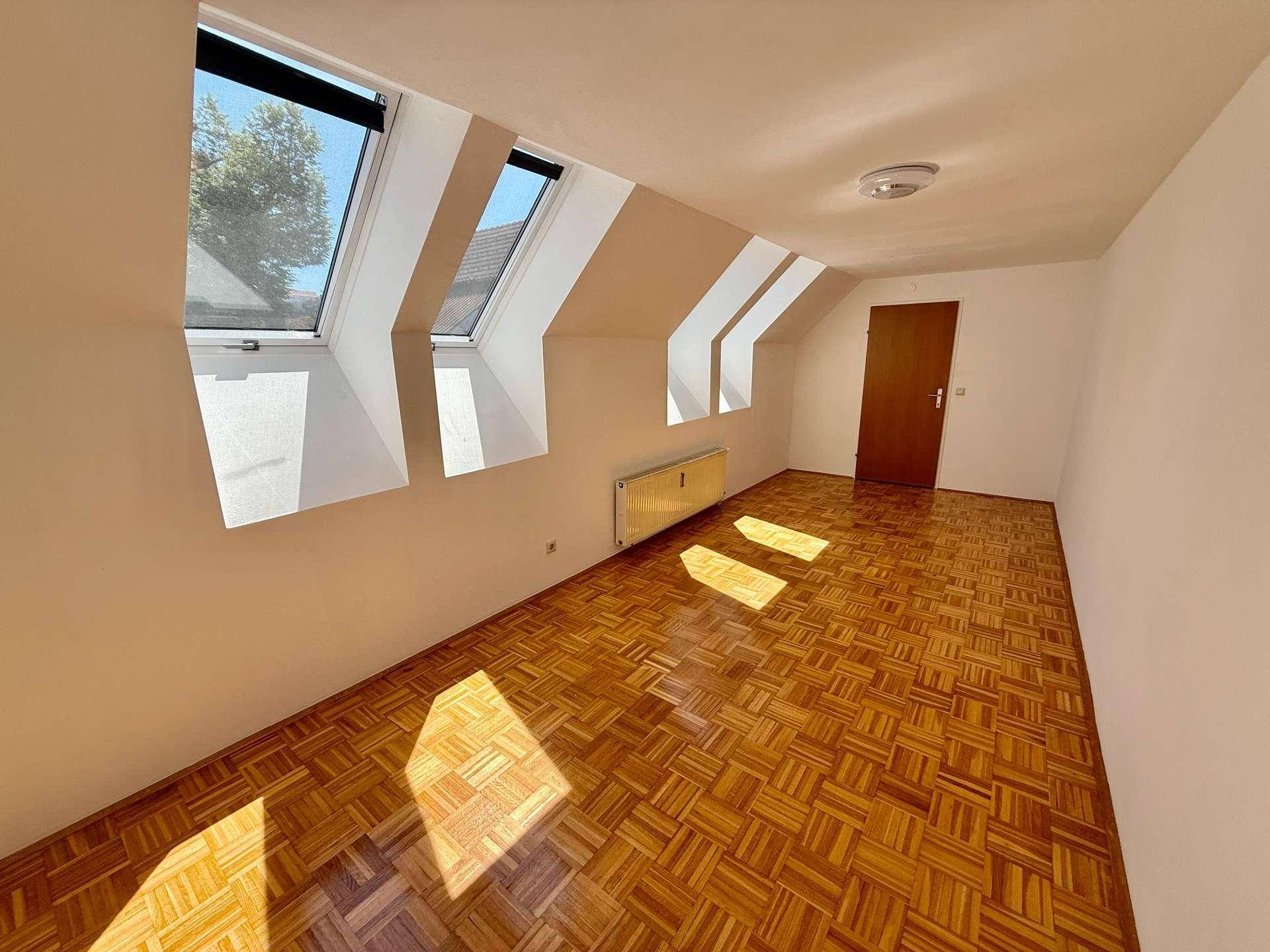 Helles Zimmer im Dachgeschoss mit Parkettboden, schrägen Wänden und Dachfenstern, die viel Licht hereinlassen.