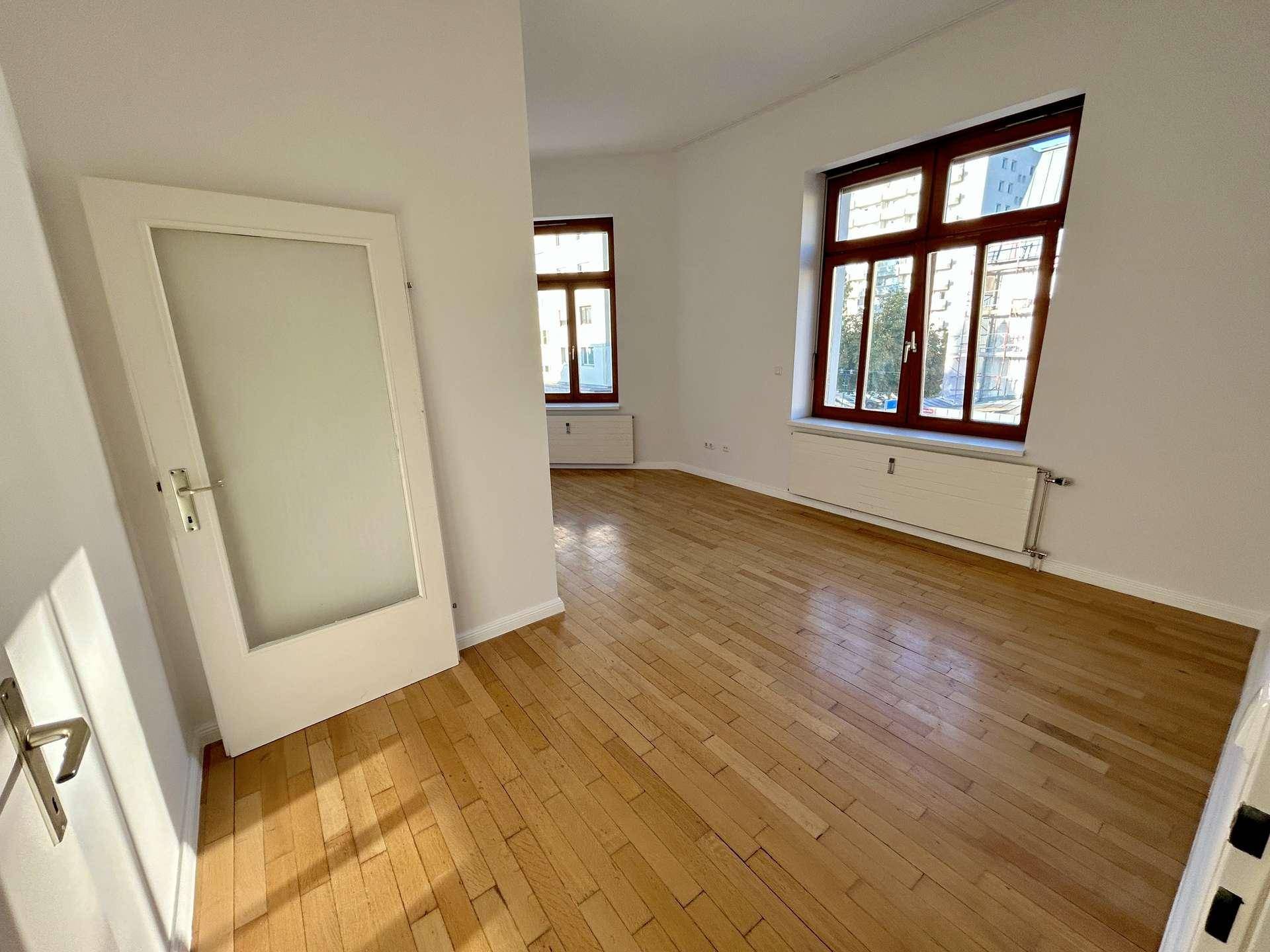 Geräumiges Zimmer mit Holzboden und großen Fenstern, die viel Tageslicht hereinlassen.