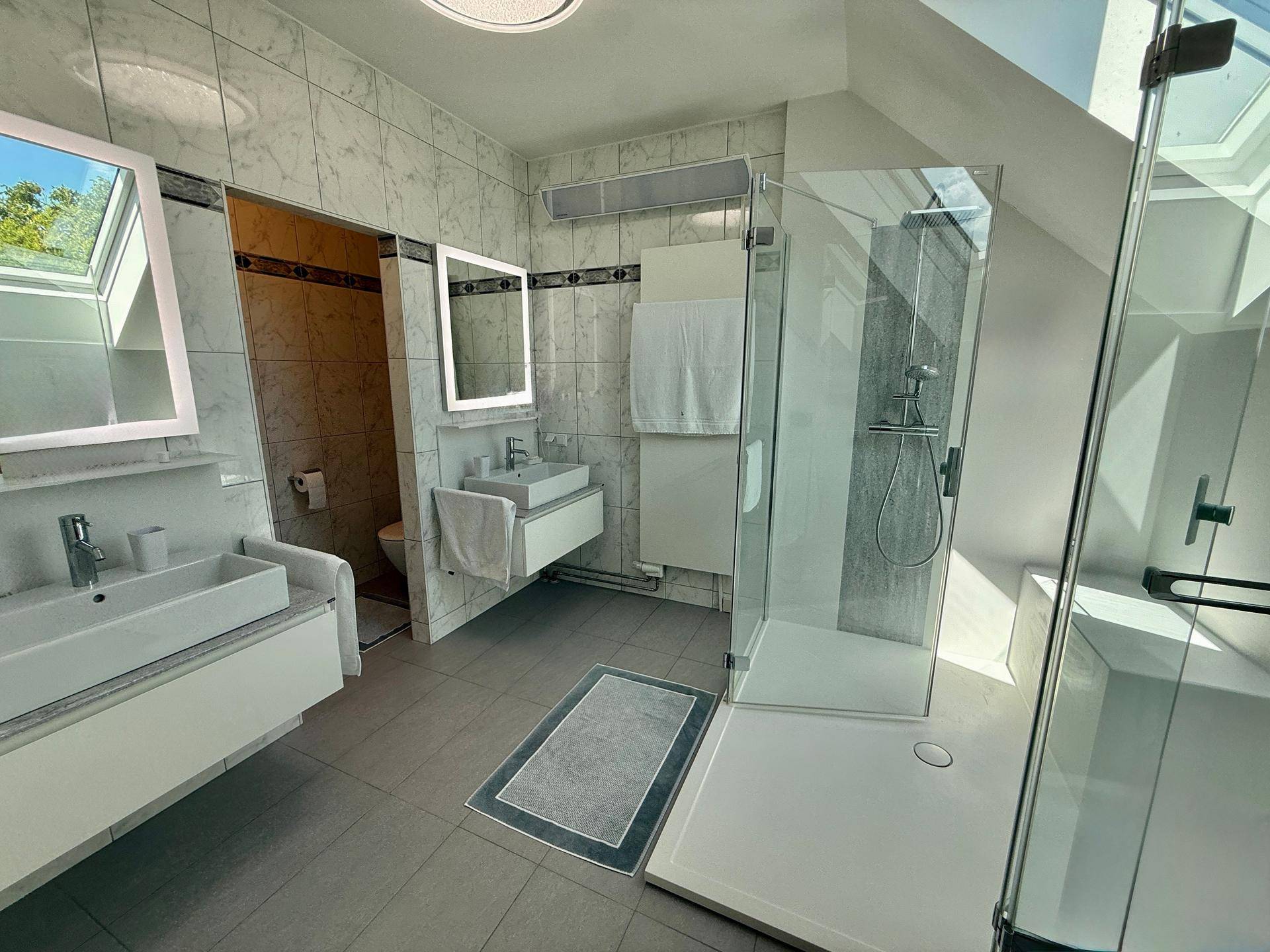 Modernes Badezimmer im Dachgeschoss mit zwei Waschbecken, Dusche und Dachfenstern.