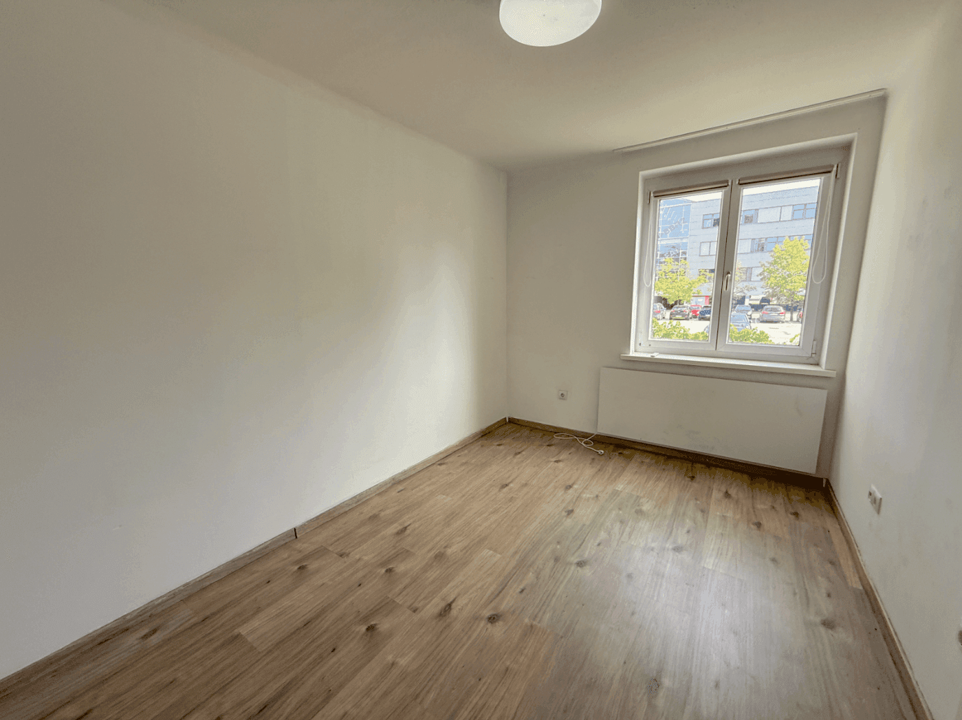 Freundliches Zimmer mit hellem Laminatboden und Blick nach draußen durch das Fenster.