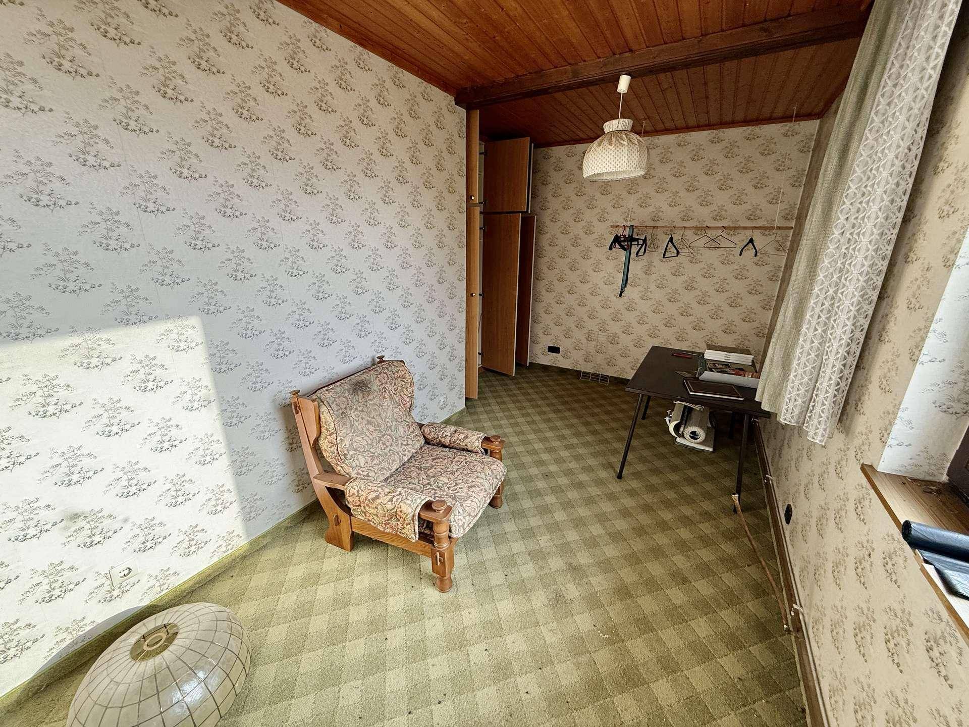 Schlafzimmer mit gemusterter Tapete, Teppichboden und Holzdecke, die eine warme Atmosphäre schafft.
