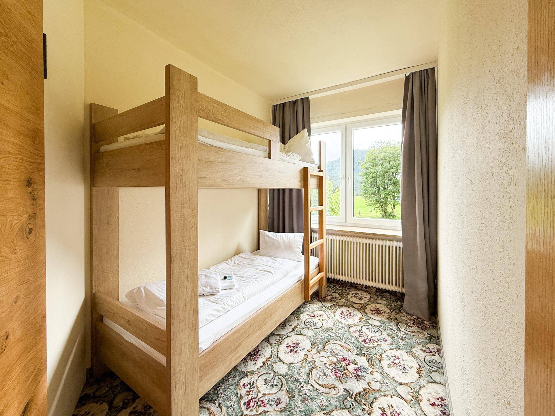 Kleines Schlafzimmer mit Etagenbett, Teppichboden und Fenster mit Blick ins Grüne.