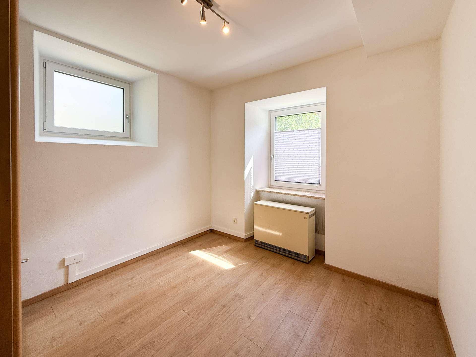 Gemütliches Schlafzimmer mit Holzboden und zwei Fenstern, die für eine helle Atmosphäre sorgen.