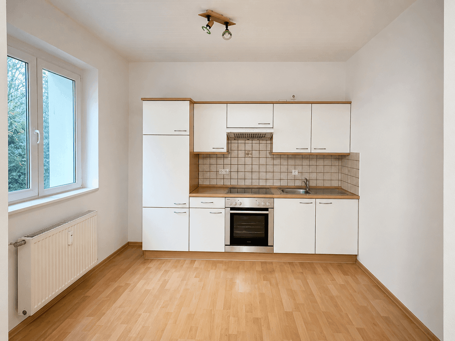 Funktionale Einbauküche mit weißen Schränken, modernen Geräten und Laminatboden.