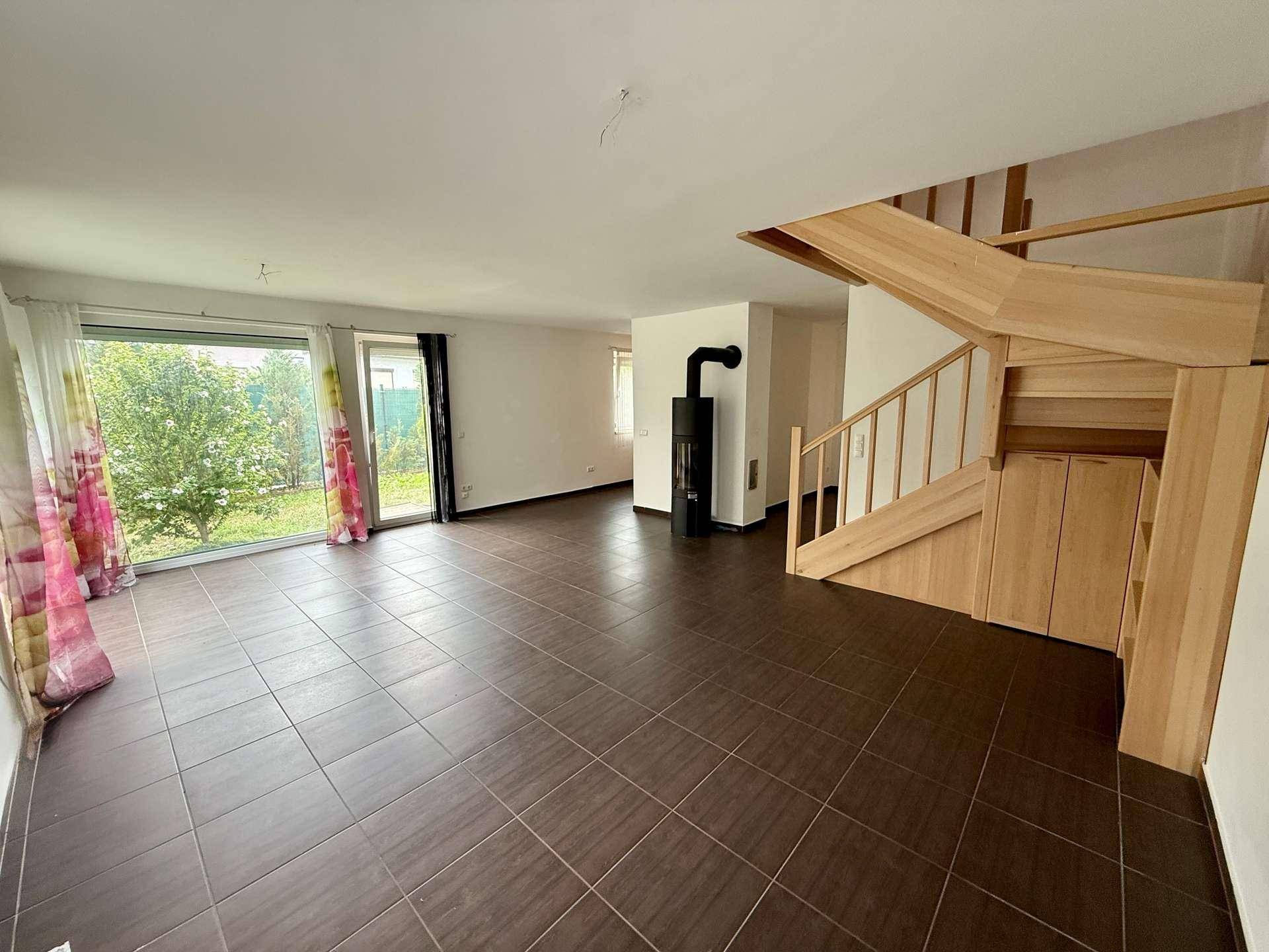 Geräumiges Wohnzimmer mit dunklen Fliesen, Holztreppe und einem modernen Kaminofen.