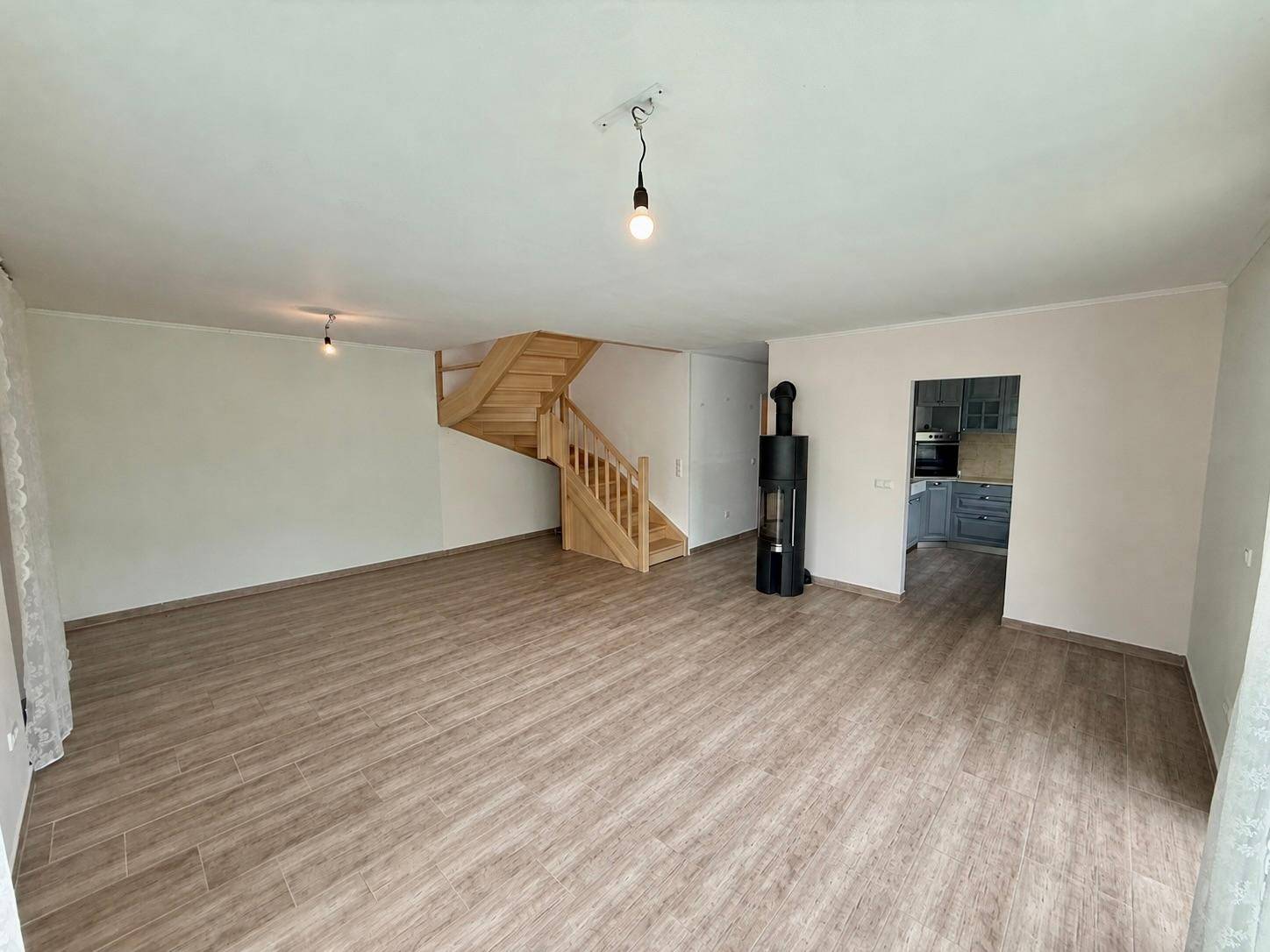 Geräumiges Wohnzimmer mit hellem Fliesenboden, Holztreppe und Zugang zur Küche.