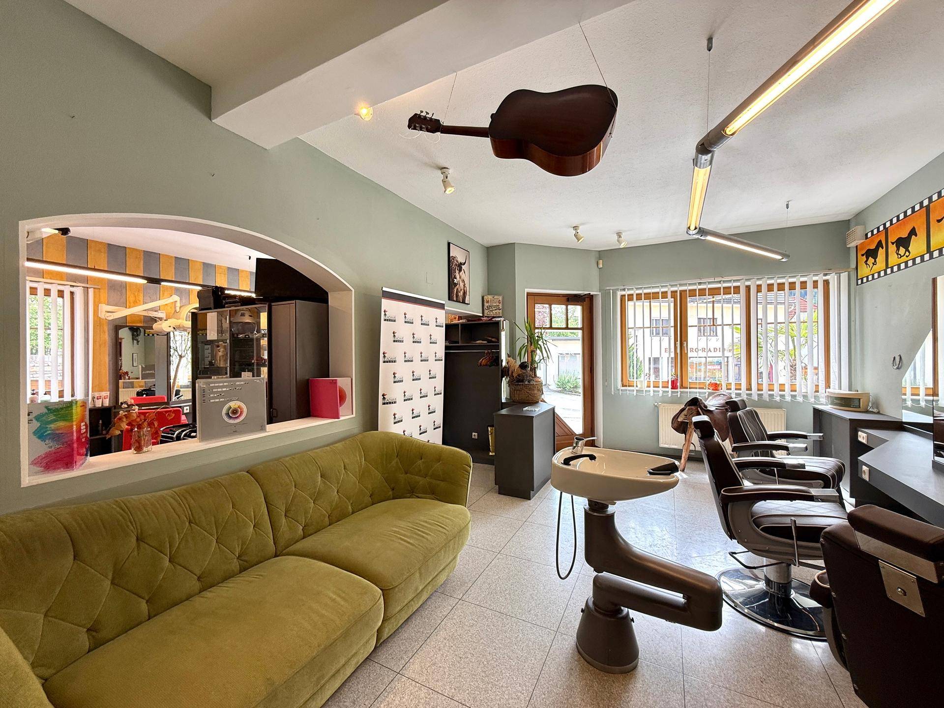 Einladender Friseursalon mit bequemer grüner Couch und Blick auf den Eingangsbereich.