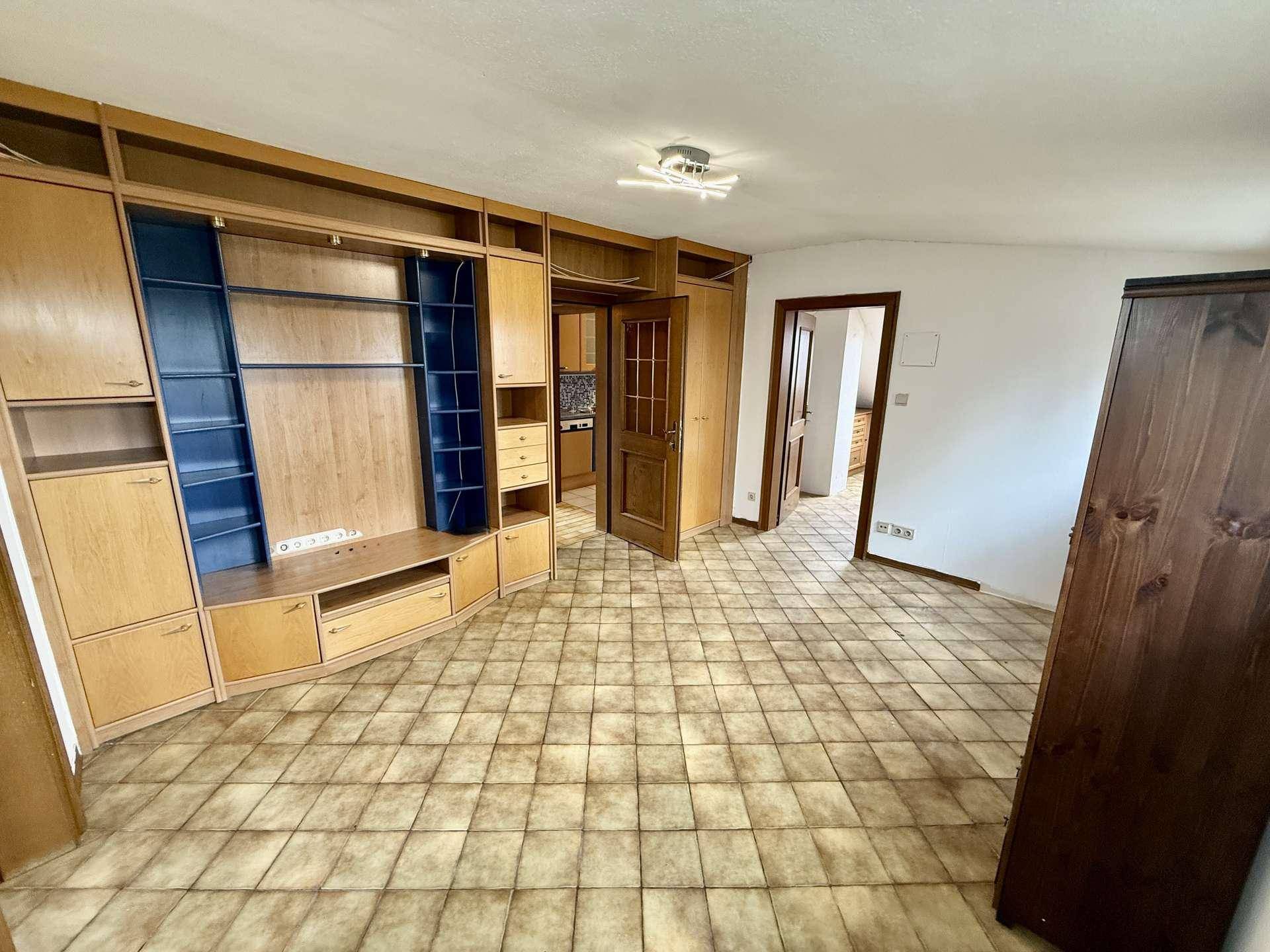 Geräumiges Dachzimmer mit großer Schrankwand und Fliesenboden.