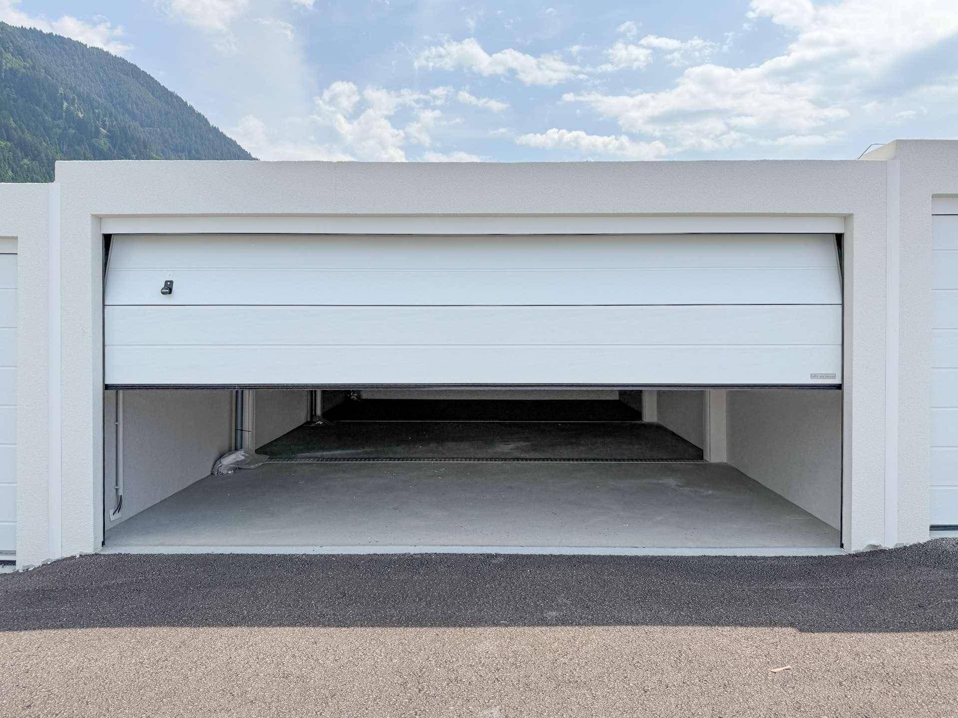 Teilweise geöffnete Garagenbox mit Blick auf den Innenraum und die Berglandschaft.